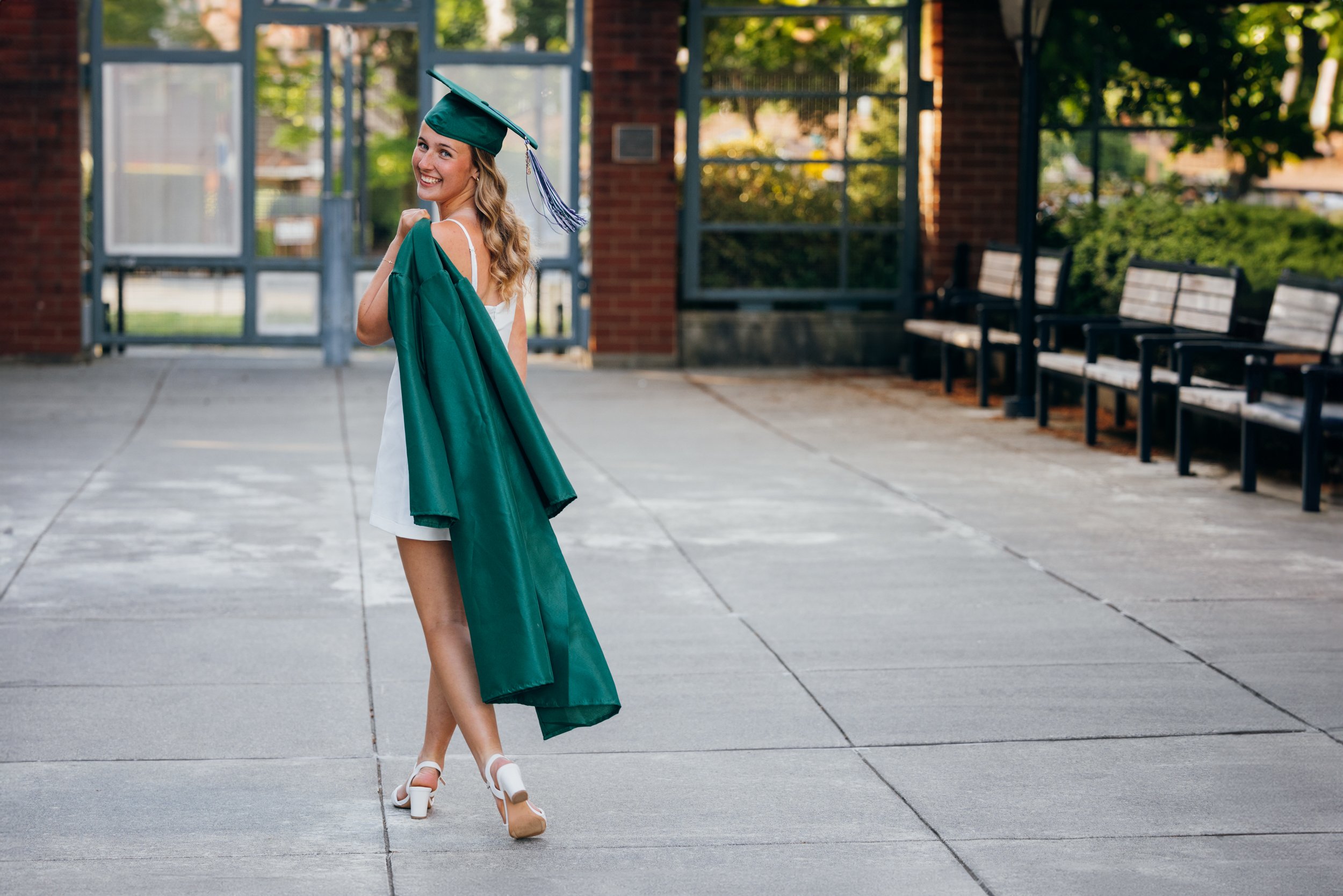  A senior walks away from the camera in her cap and gown, the gown is slung over her shoulder.  She is at her school in Edmonds Washington.  