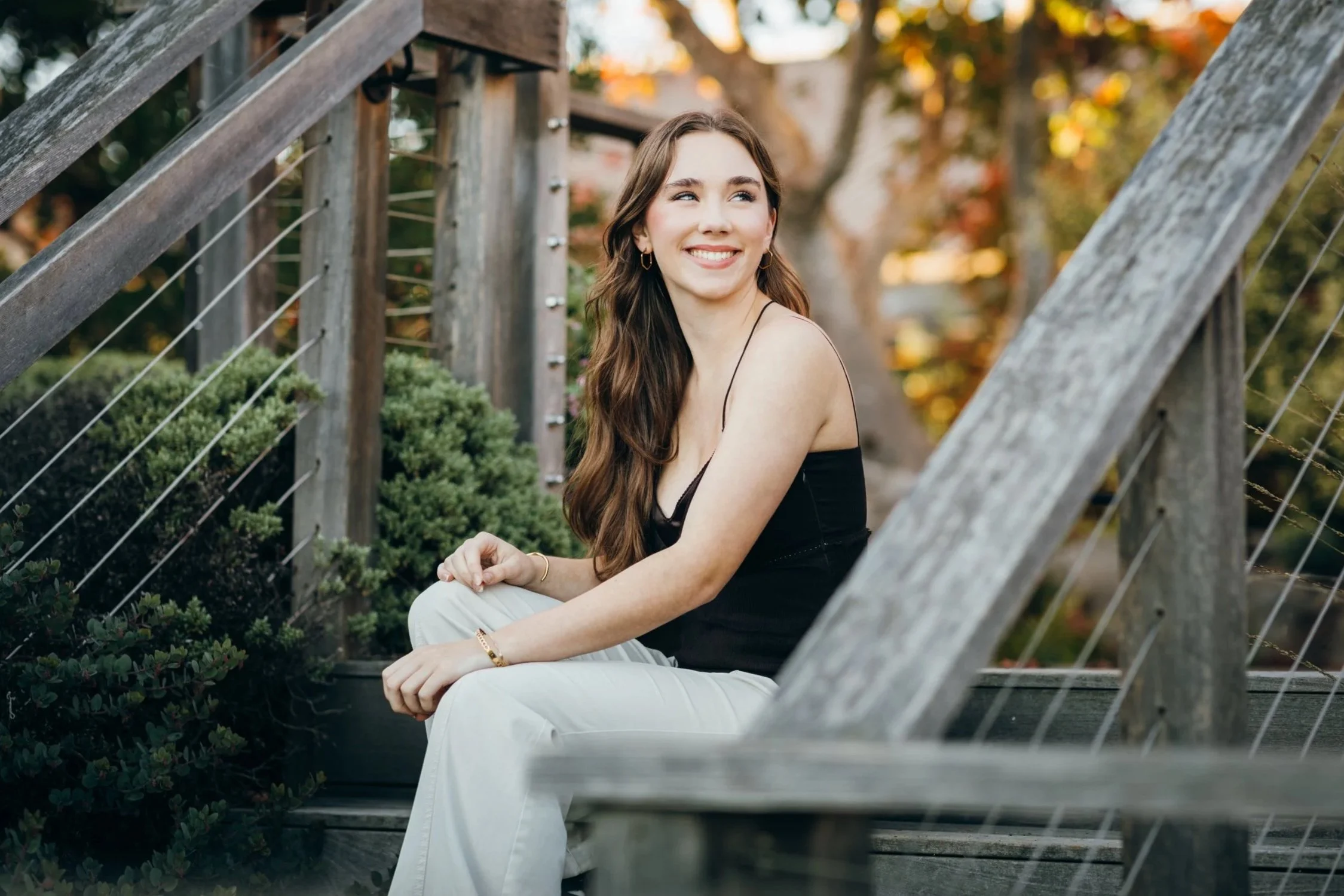 Senior girl with long brown hair sitting on steps, fall leaves in background