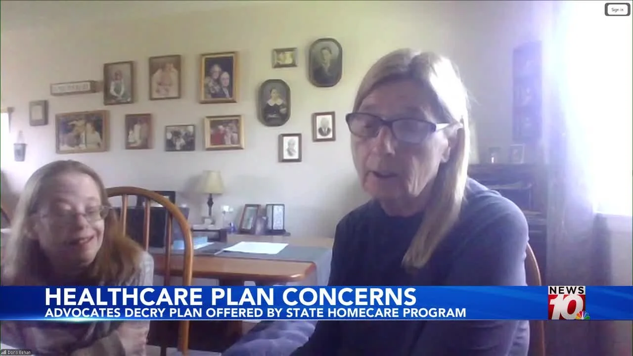 An older woman and younger disabled daughter talk to reporters. There is news 10 banner across the bottom reading Healthcare Plan Concerns: Advocates Decry Plan Offered By State Homecare Pr. There are lots of photographs on the wall in the background
