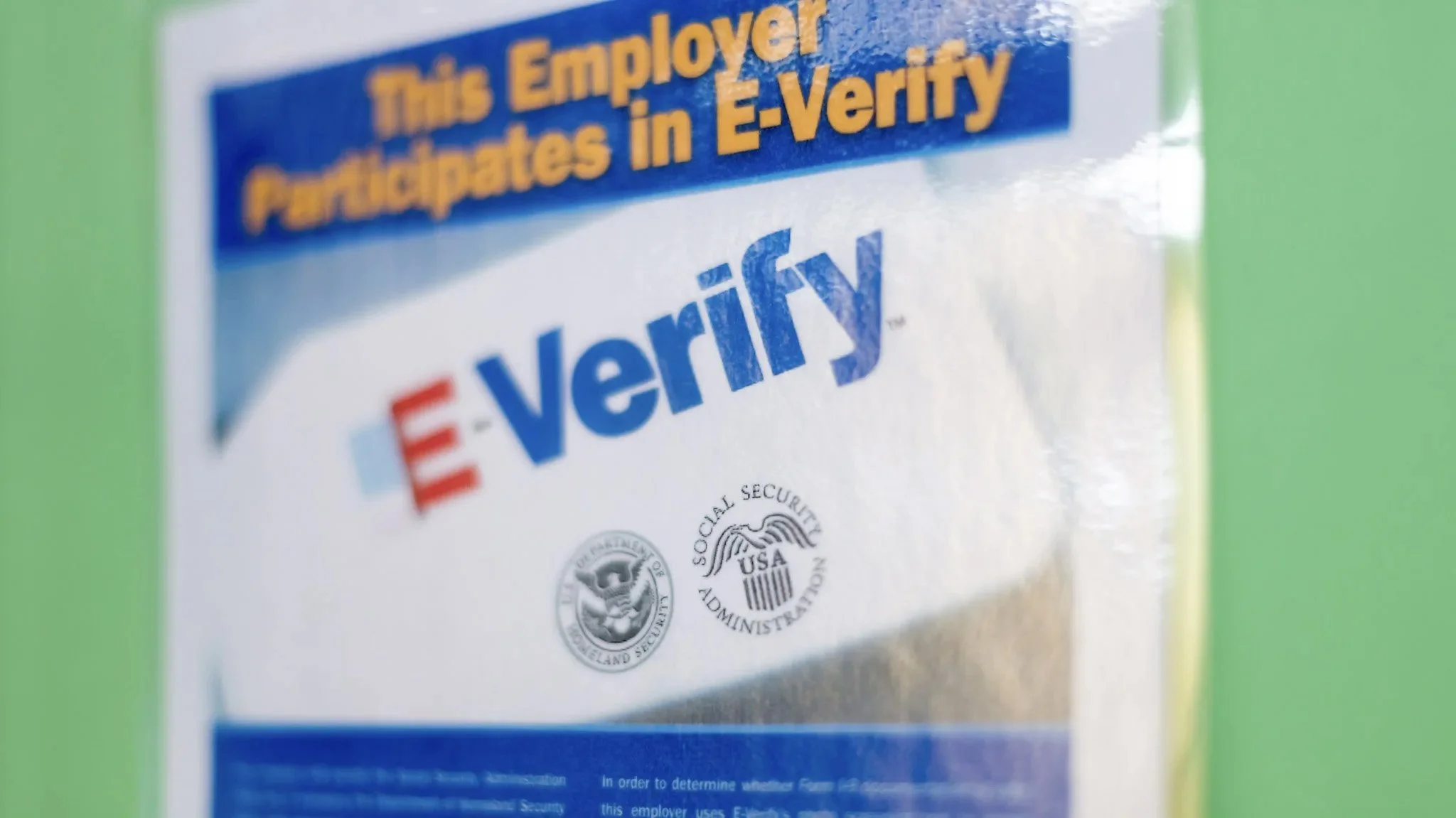 A stock photo of a sign that reads "This Employer Participates in E-Verify"