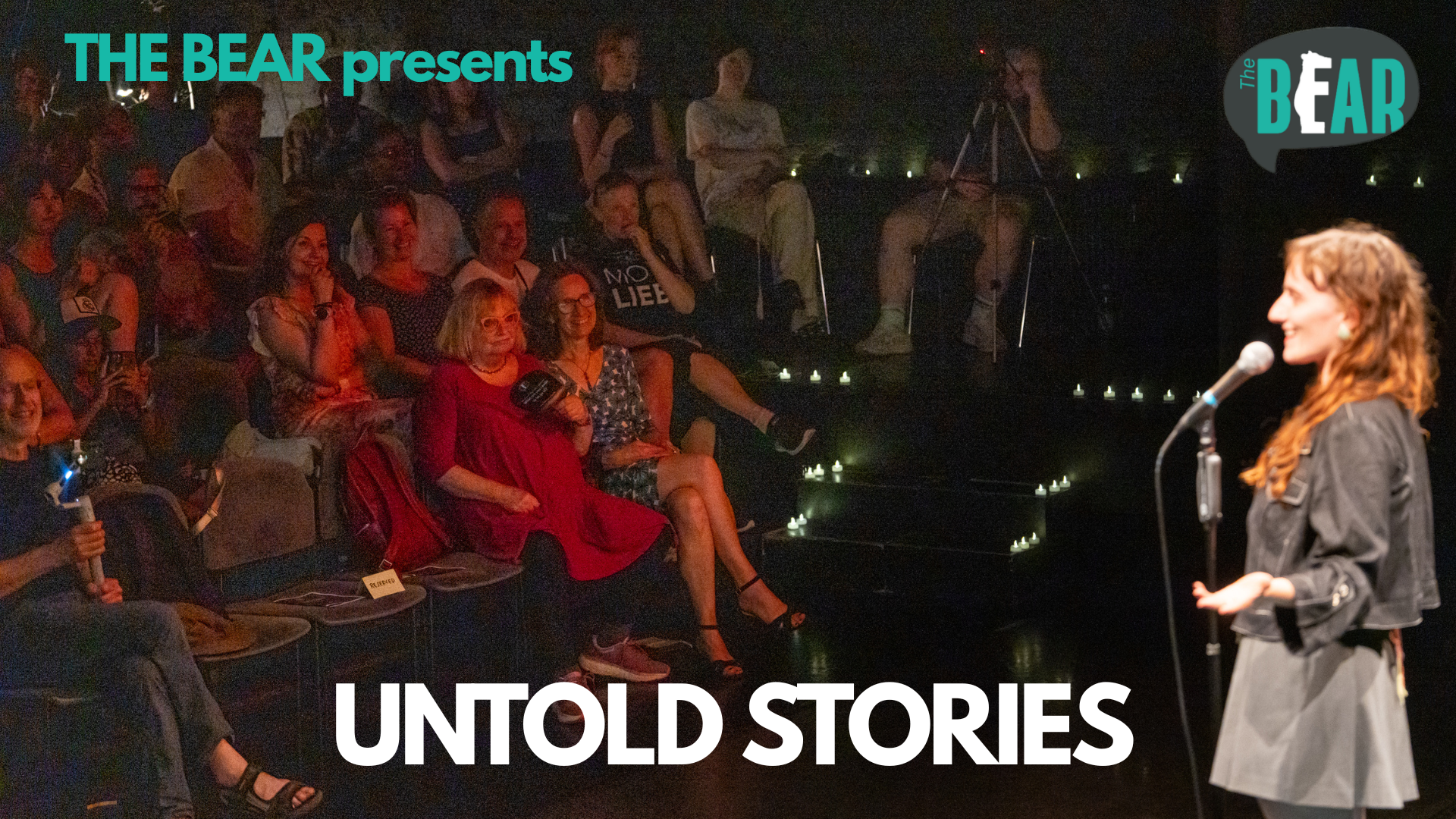 Storyteller performing on stage at THE BEAR's Untold Stories event in Berlin, with audience seated around candlelit steps