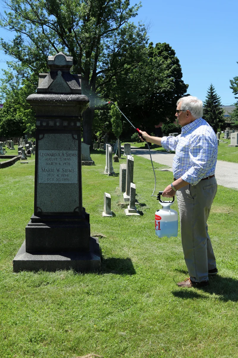 Dying to Tell Their Stories blog author Richard Berglund removing lichens and moss from his maternal great-great grandparents' grave stone in Green Mount Cemetery.