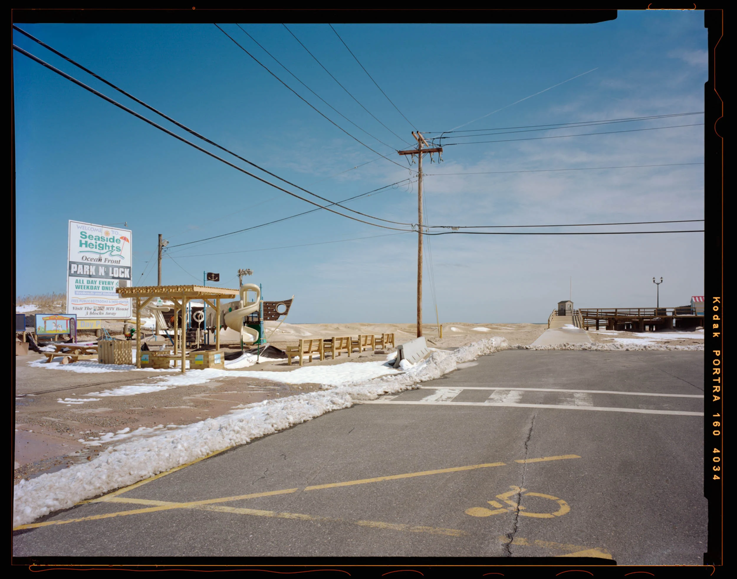 Park and Ride, Seaside, NJ. 2014. 4x5 Negative Shen-Hao This photograph was the 3rd photograph I took for this entire project. It was right in December before I went back to school and started really getting this project rolling. This image anchors the entire symbolic meaning of the project. The kids’ playground covered in snow with the bright sunny sign behind it. The entry of the boardwalk inviting you in with the telephone pole splitting the entire image. The North end of the boardwalk being re-built. The dunes pushed up to boardwalk in the background from the hurricane. The handy cap symbol foreshadowing the state of the boardwalk.