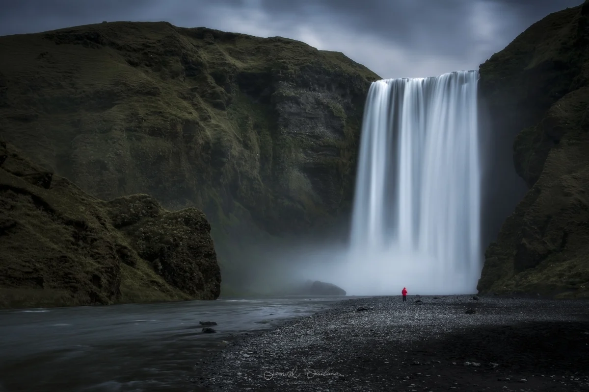 A lone tourist stands beneath the mighty Skogafoss waterfall.