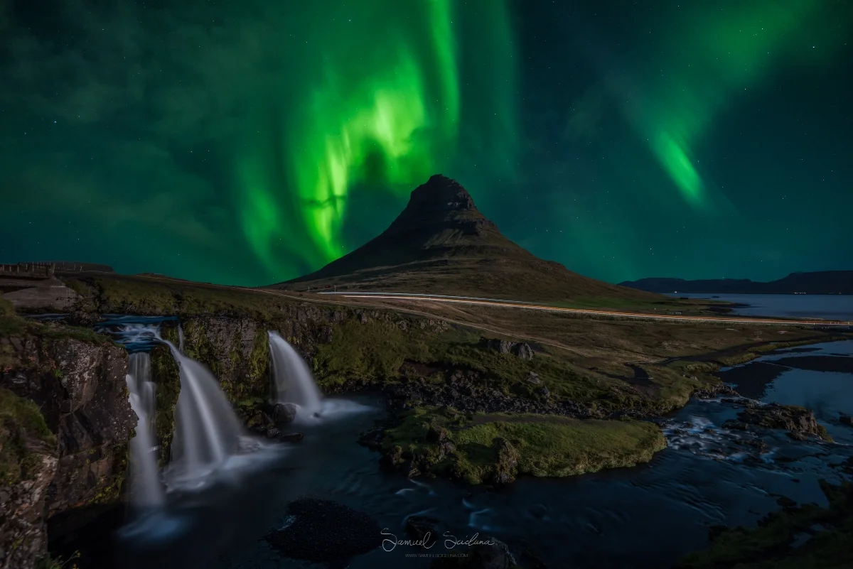 Thin clouds roll in as the Northern lights dance above Kirkjufell mountain.