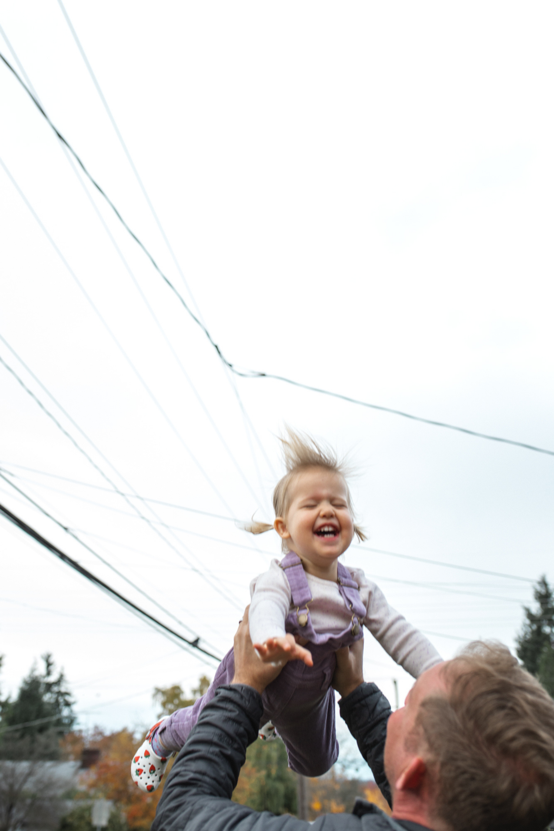 Photograph of a toddler at home in seattle being tossed in the air by her dad