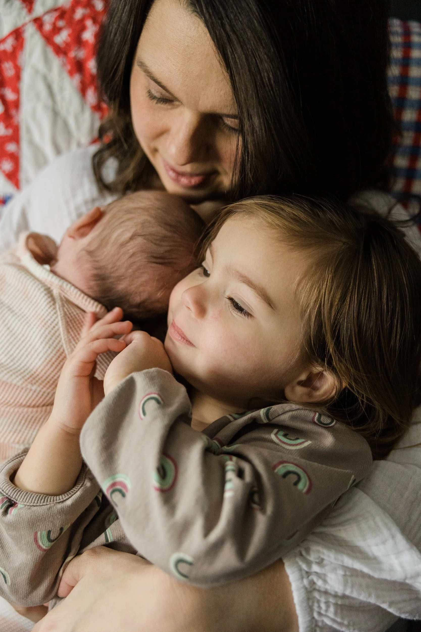 close up on faces of mom holding baby and small girl against her chest