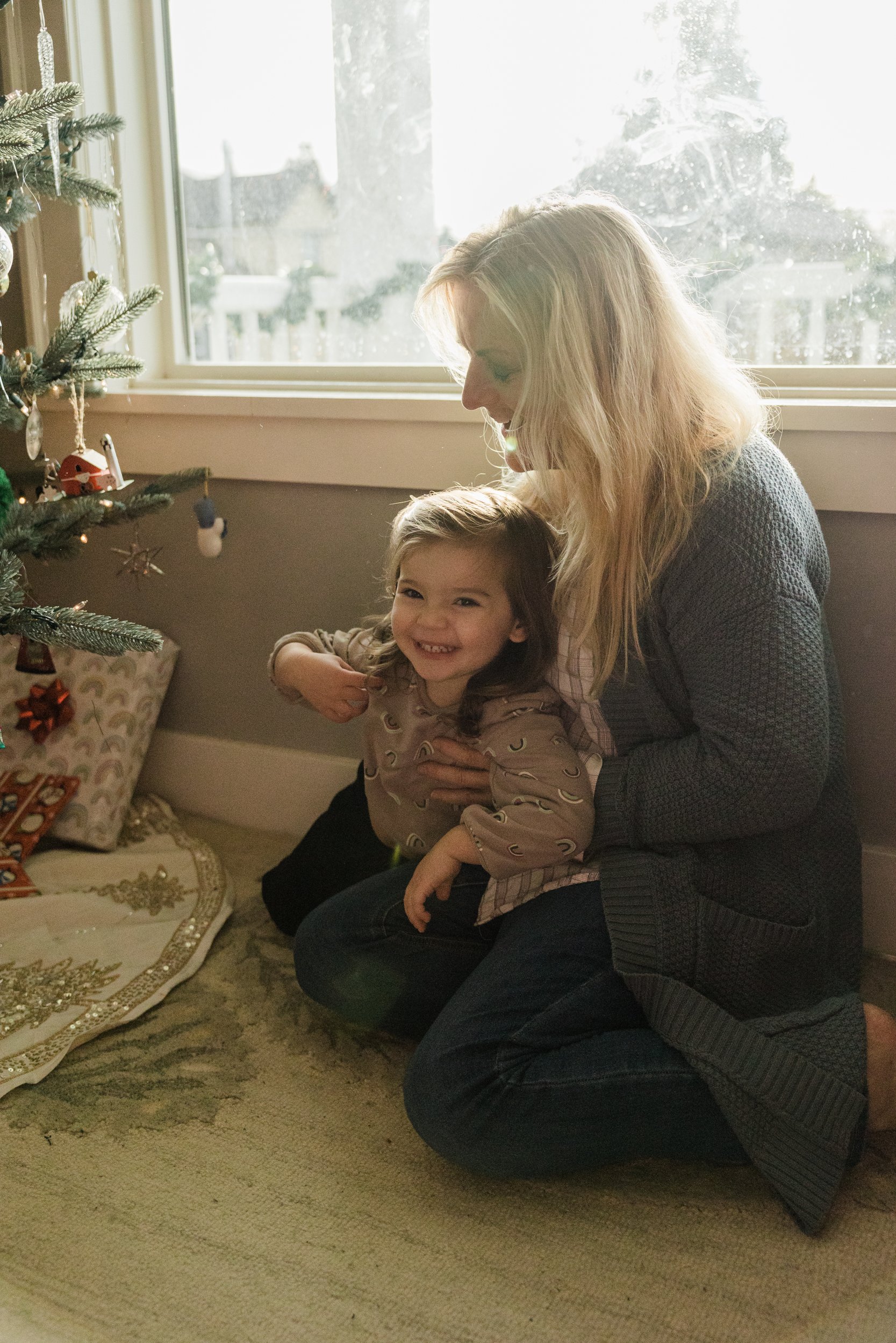 older woman and little girl sit next to a christmas tree