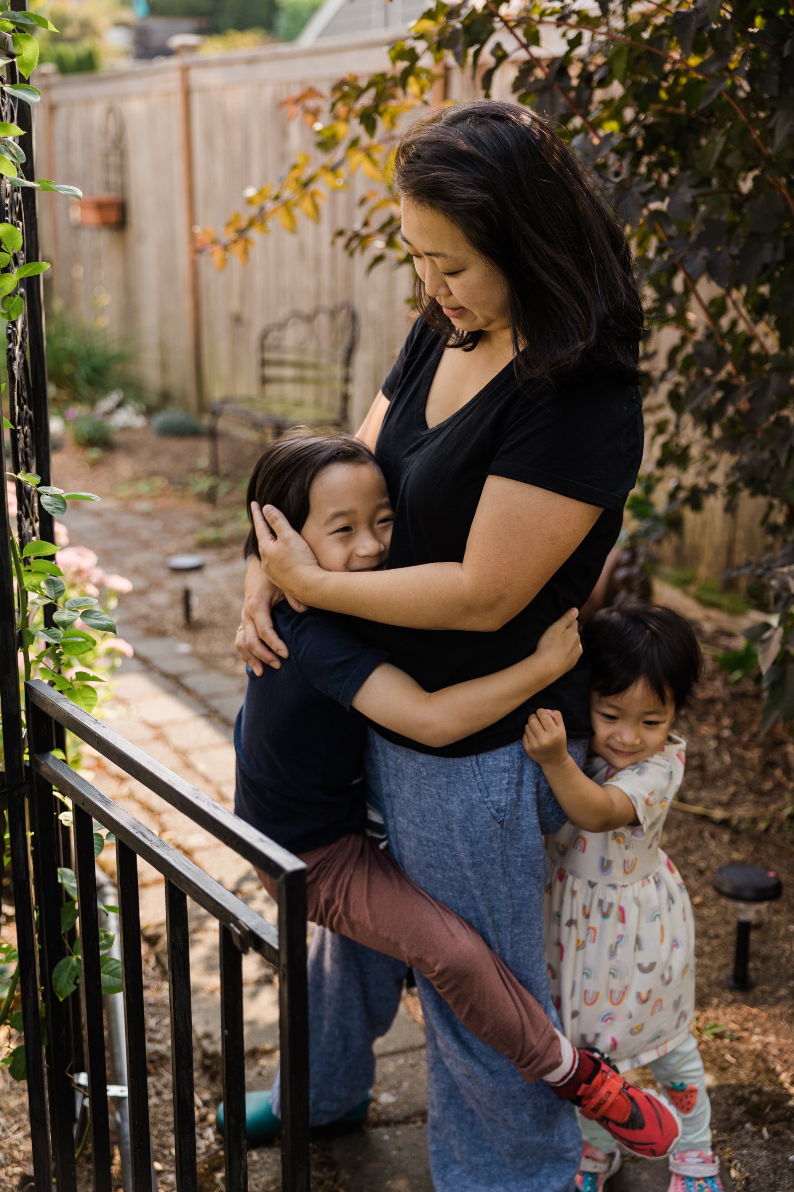 mother hugs child while another child hugs her legs from behind outside