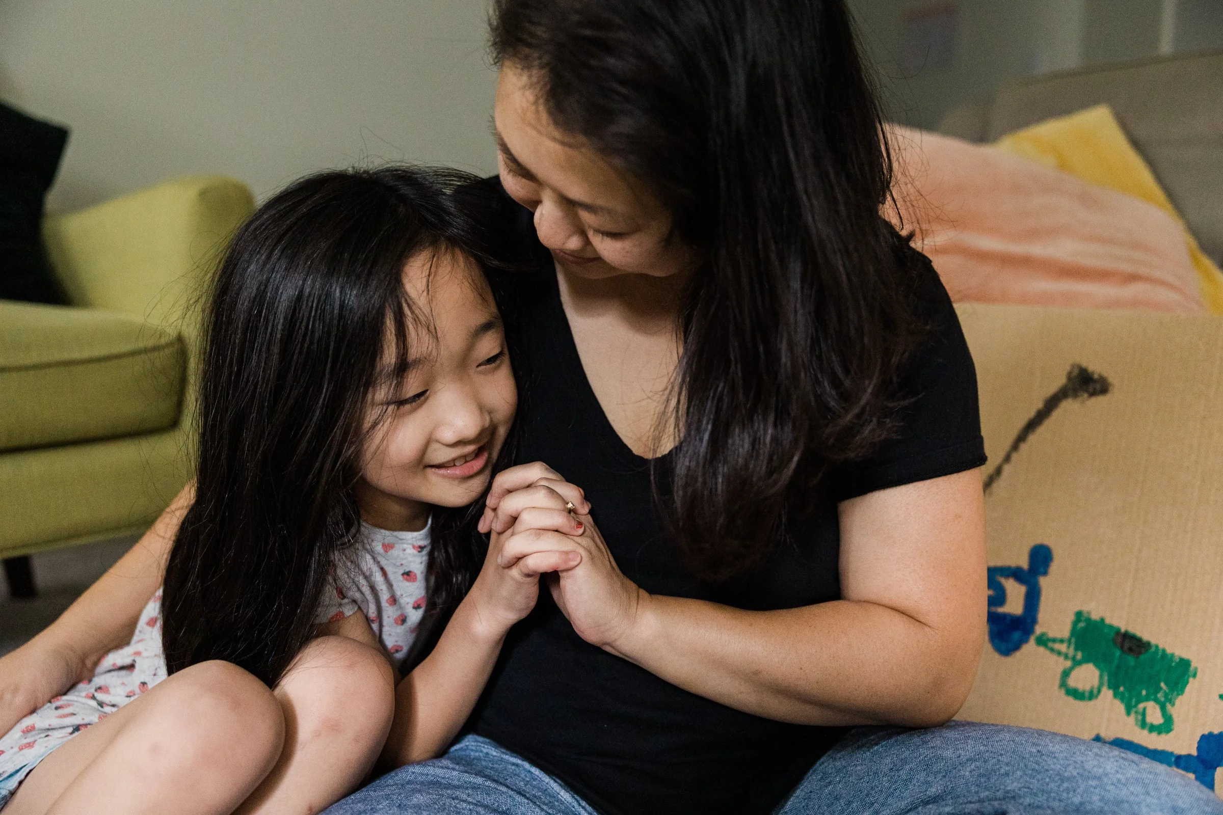 mother and daughter interlock fingers while snuggling on the floor