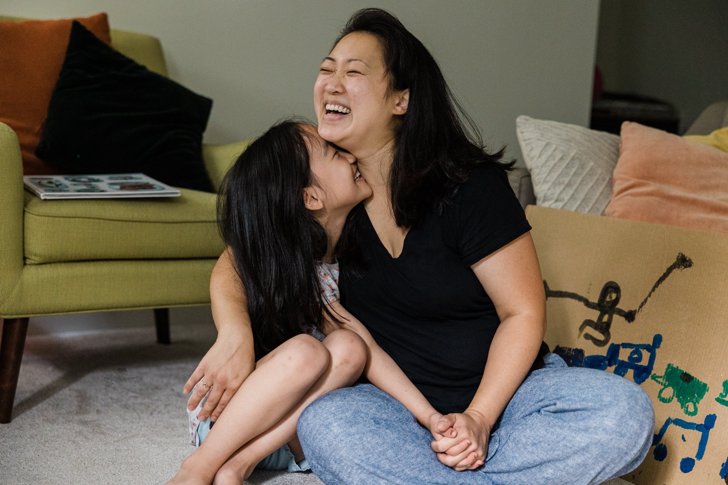 daughter snuggles mother's neck while they hug on floor