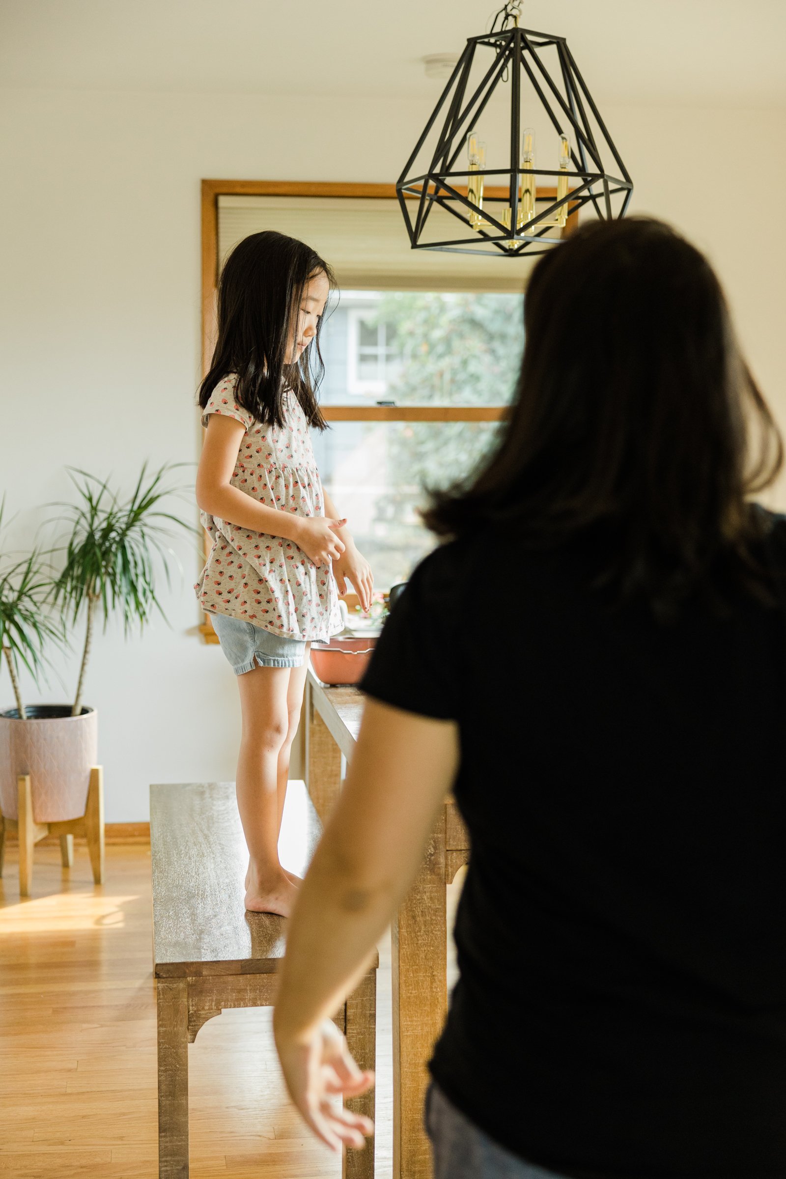 elementary school girl stands on wooden bench with mother in the foreground