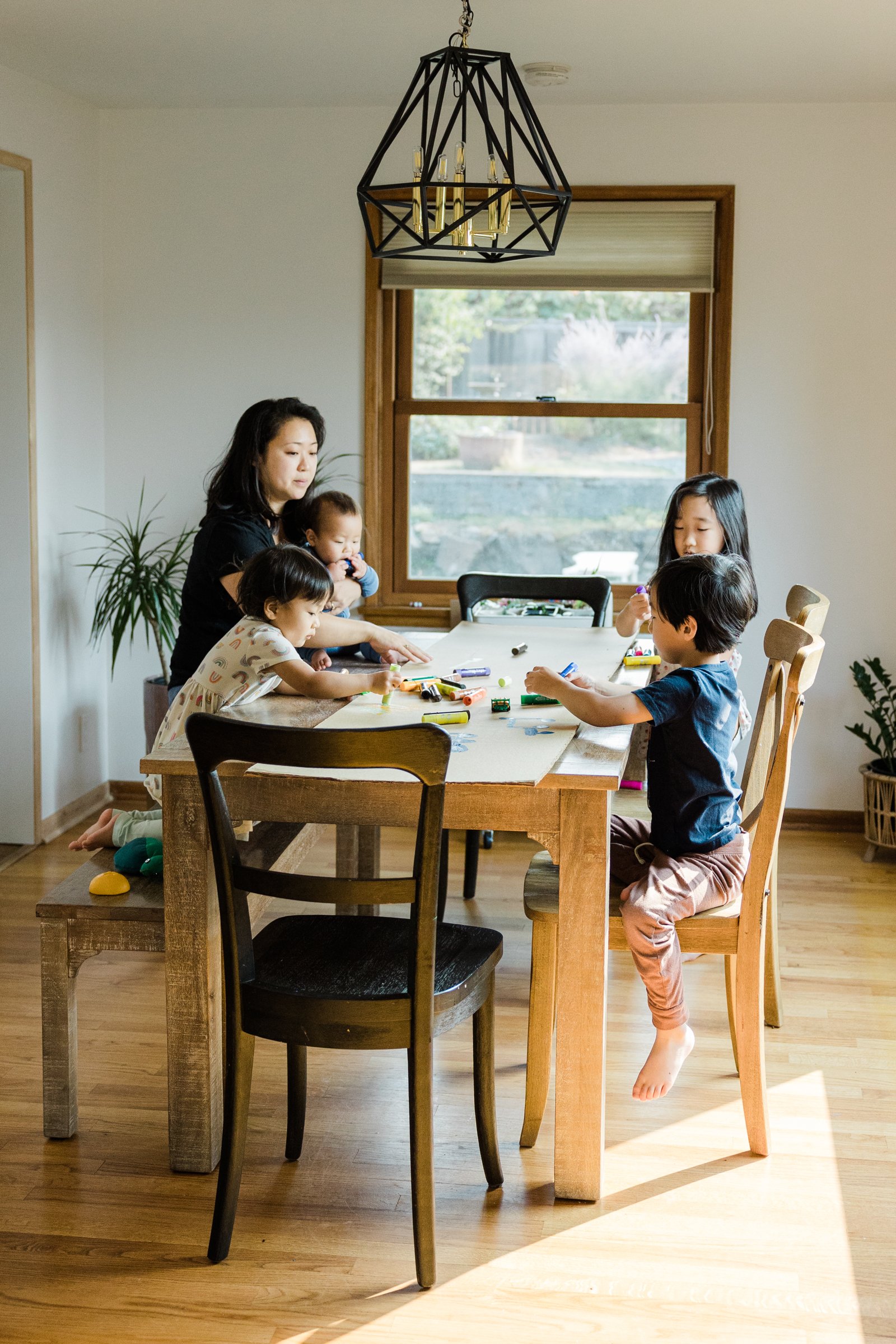 mother with four children sits at wooden dining room table drawing on cardboard