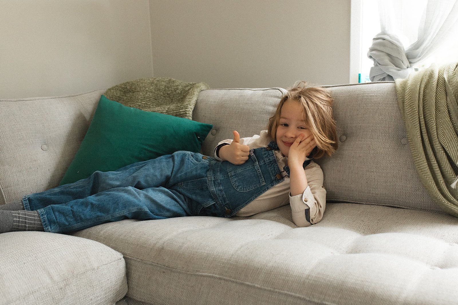 little boy lounges on his side on couch while giving a thumbs up