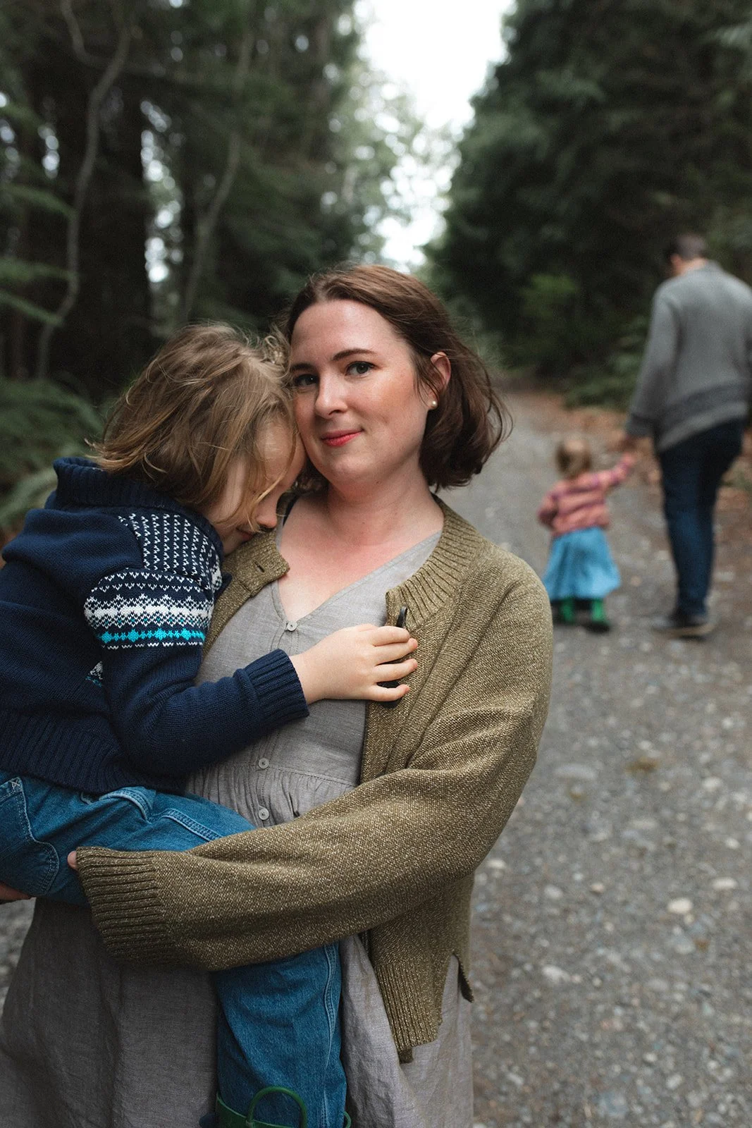 son nuzzles his mom's neck while father and daughter walk behind them