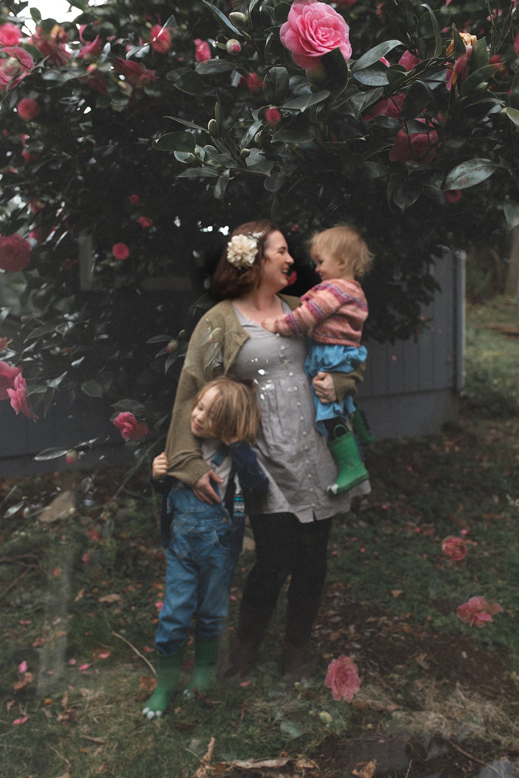 double exposure, mother holds little girl in arms and little boy on ground, images of flowers are lightly overlayed this image