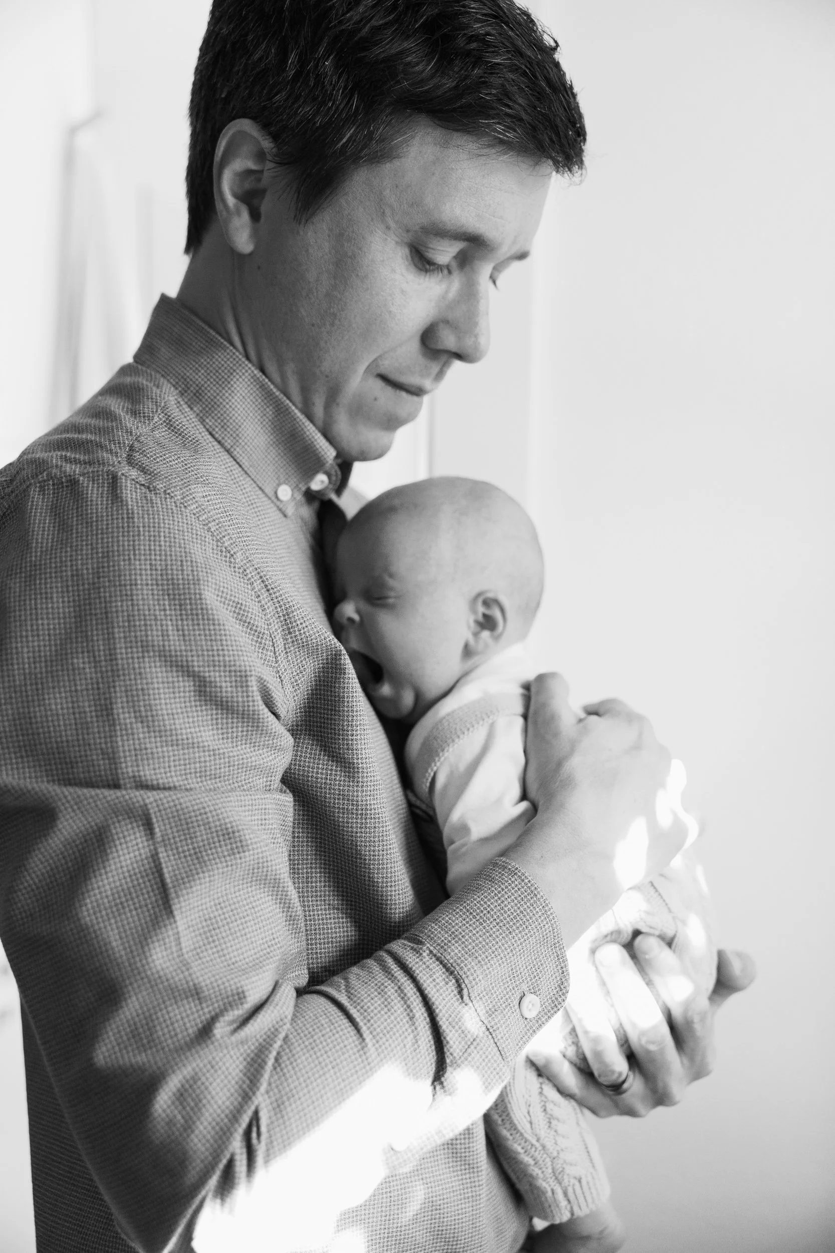 Dad hols newborn who yawns during family photos