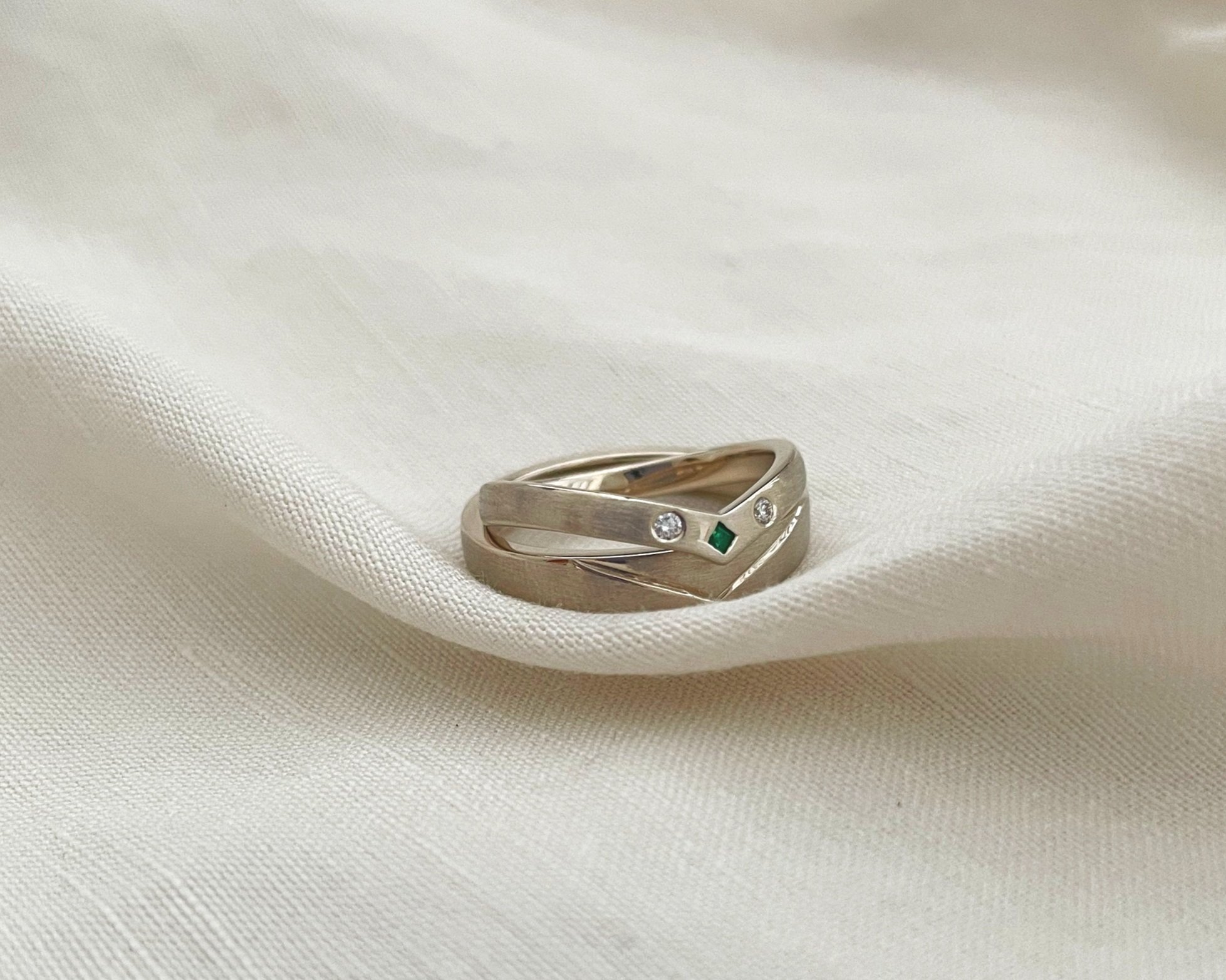  A pair of wedding bands that fit perfectly in a V shaped groove. The top band is set with Diamonds and an Emerald 