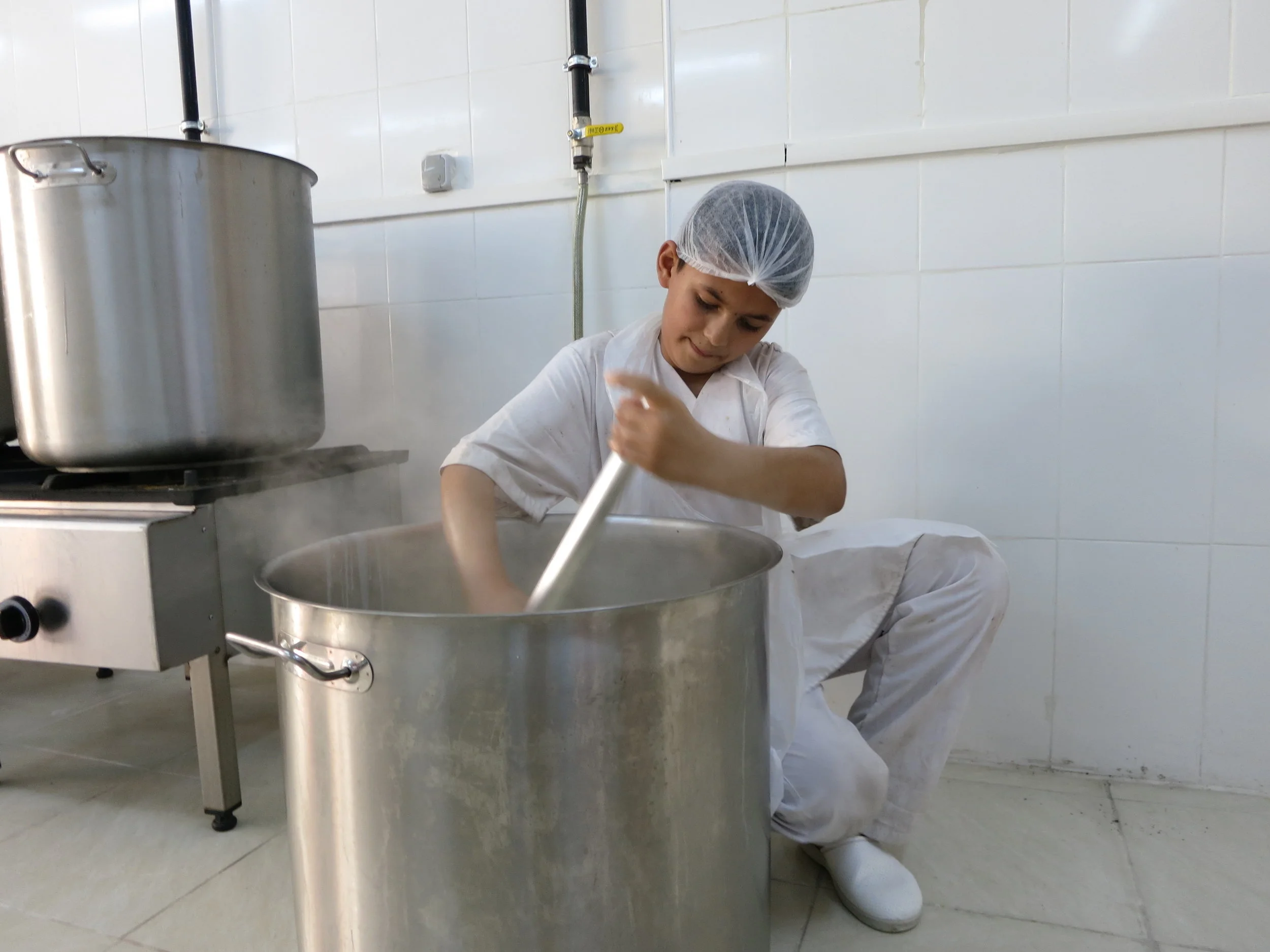 Rubi, 12 here, stirs a pot of steaming milk to make Salloura's iconic fresh cream for its desserts. (Photo by Lauren Bohn)