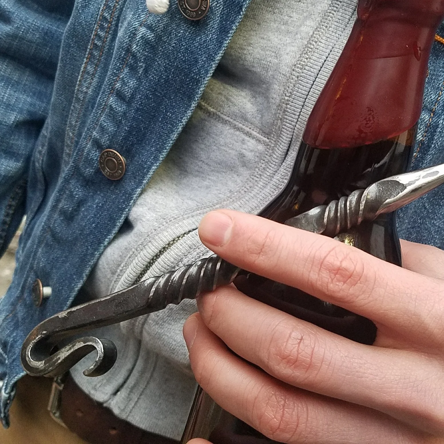 Hand forged, hand ground bottle opener complete with serrated edge for opening wax dipped bottles. Shown here held and ready to use.