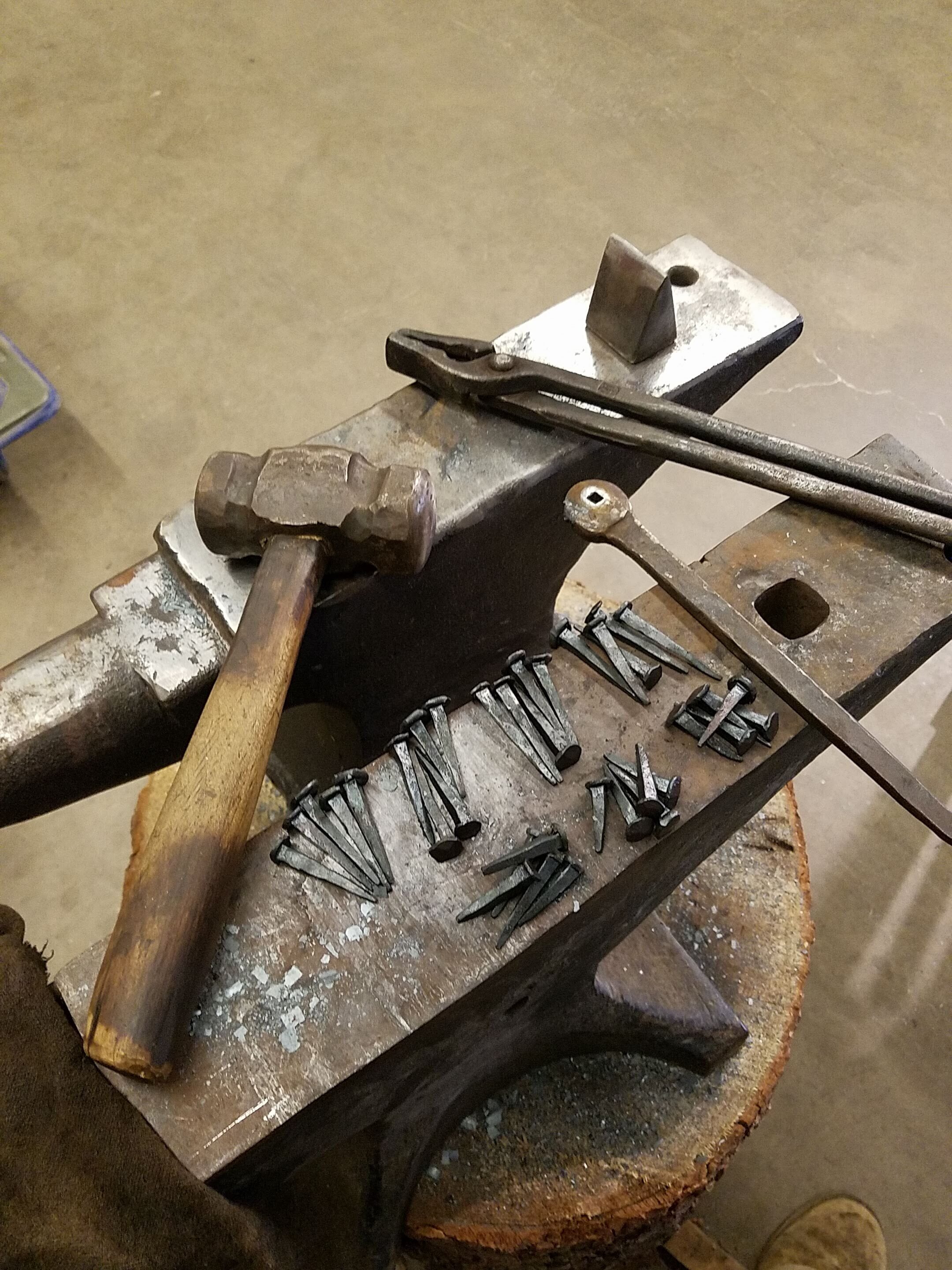 A collection of Blacksmithing Tools, including a hammer, tongs, nail header and freshly made nails