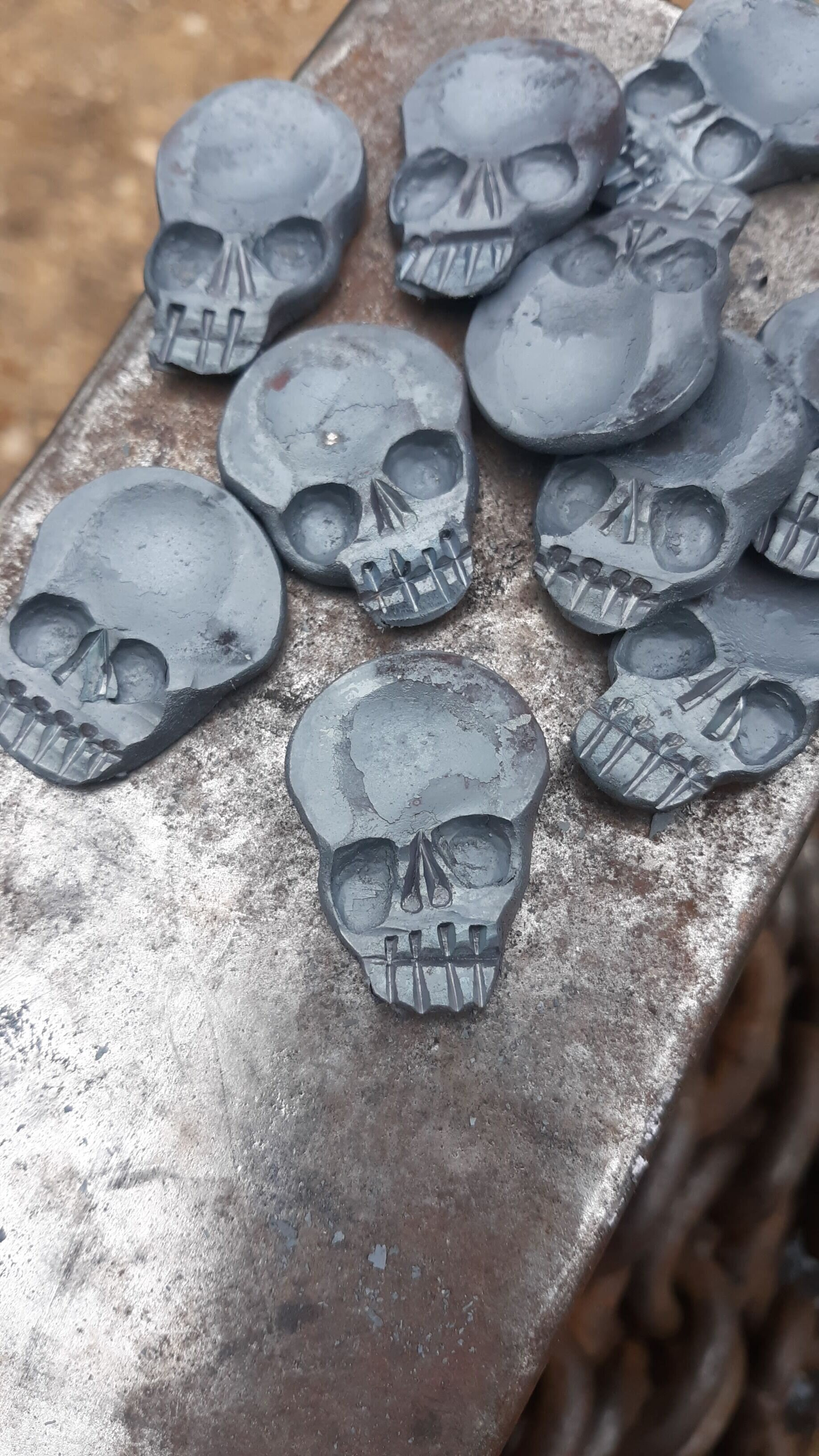 A "Memento Mori" worry coin, hand forged from 3/4" round stock steel and shaped in the form of a skull. Shown here as many coins resting atop the anvil.