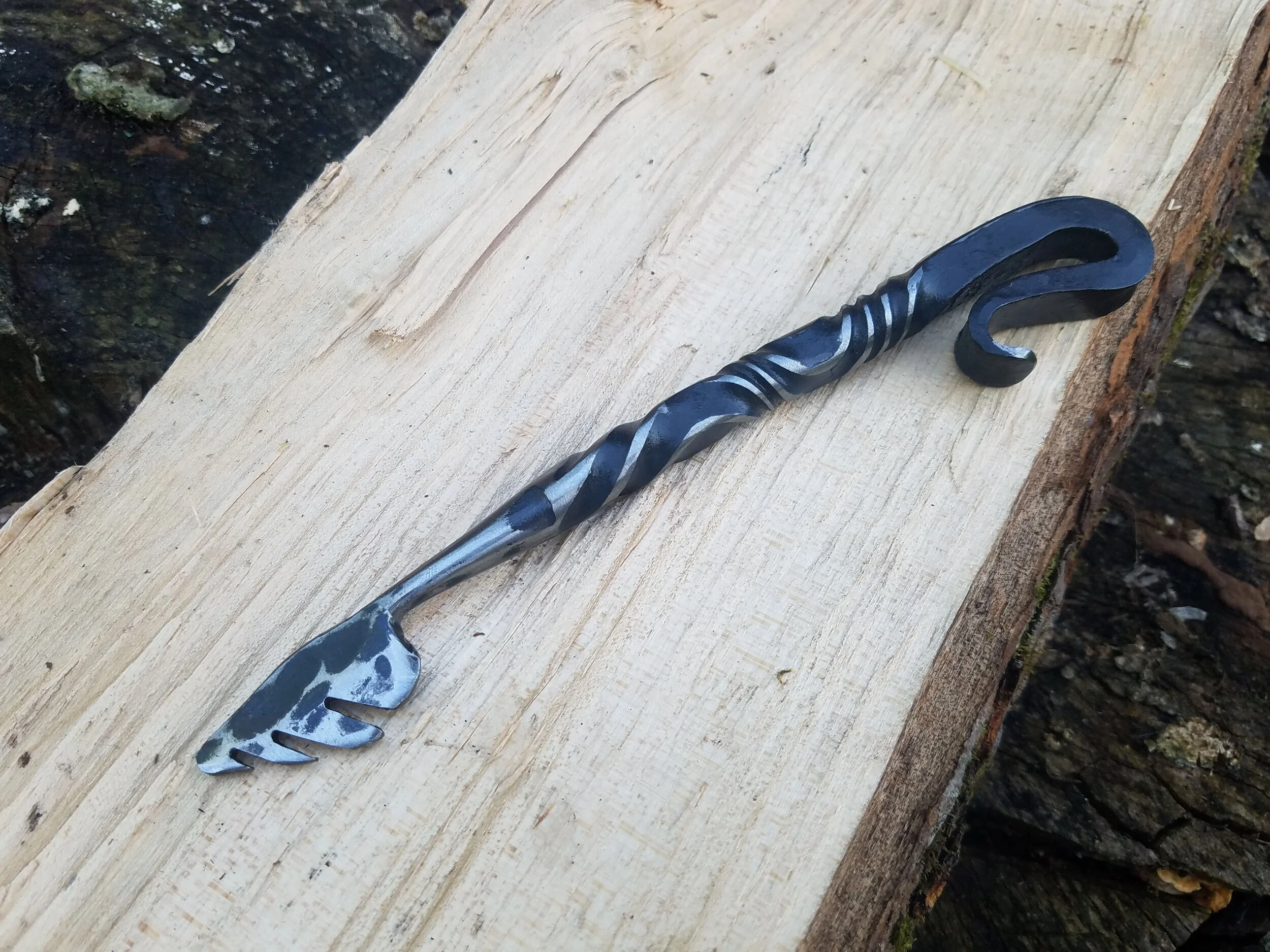 Hand forged, hand ground bottle opener complete with serrated edge for opening wax dipped bottles. Shown here resting on wood.