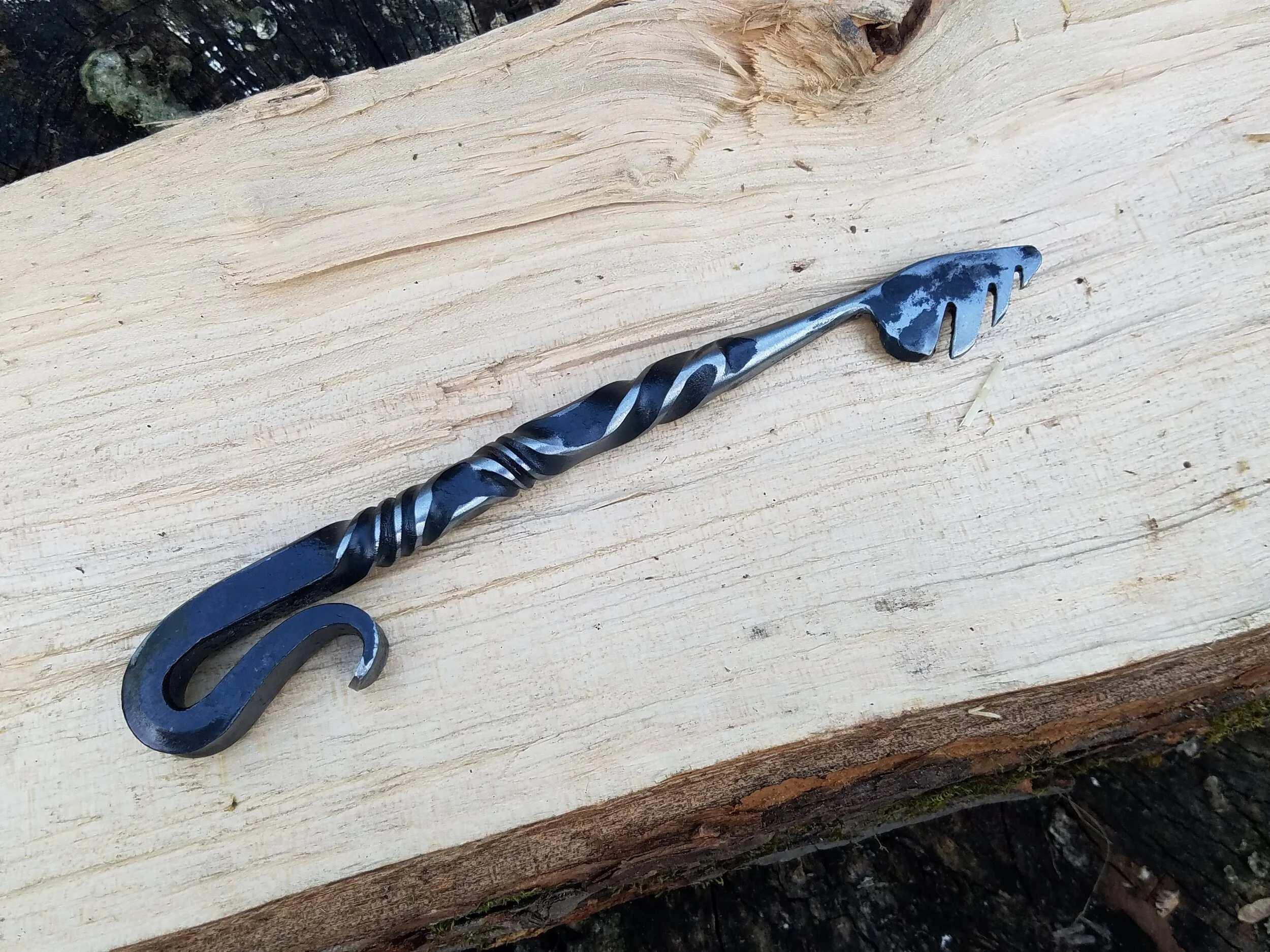 Hand forged, hand ground bottle opener complete with serrated edge for opening wax dipped bottles. Shown here resting on wood.