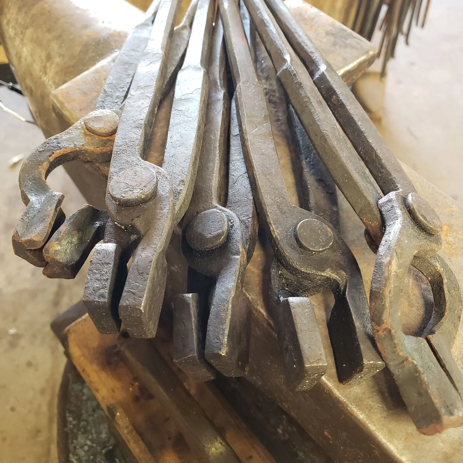 A set of large, rusty metal tongs placed on a workbench in a blacksmith shop.