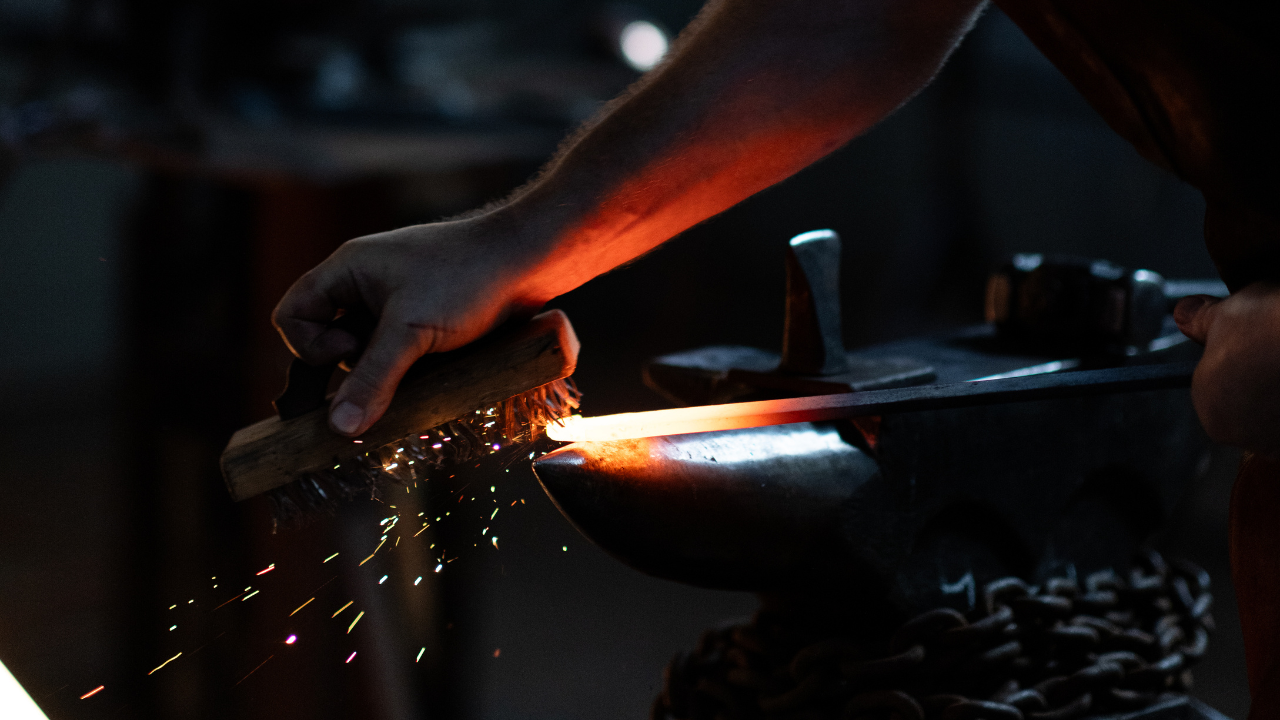 Blacksmith heating and shaping metal with a forge, sparks flying as the metal is worked.