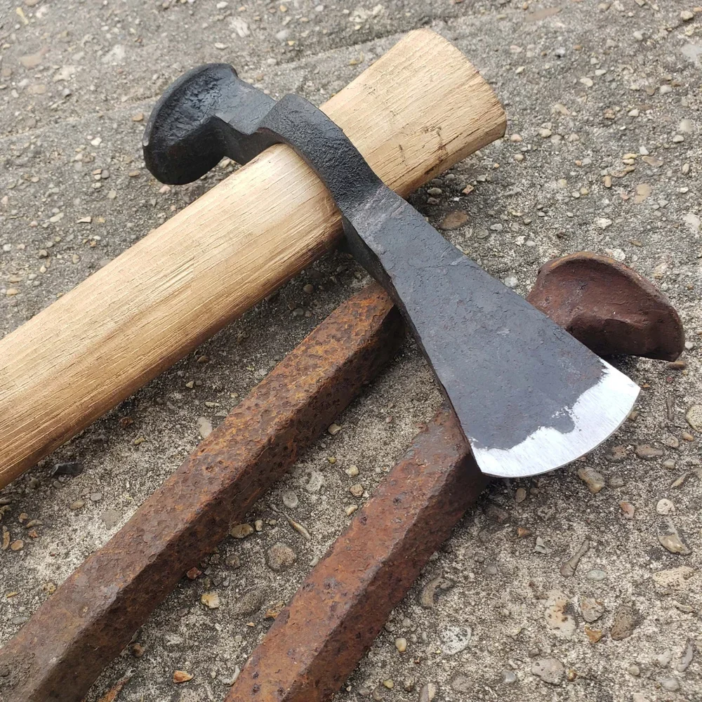 A hammer resting on a wooden log, with rusted metal rails and a worn railway spike in the background.