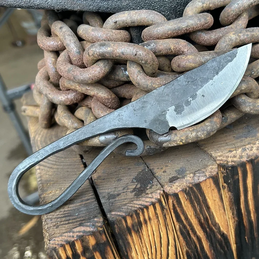 A metal knife with a curved blade resting on a rusty chain on a wooden surface.
