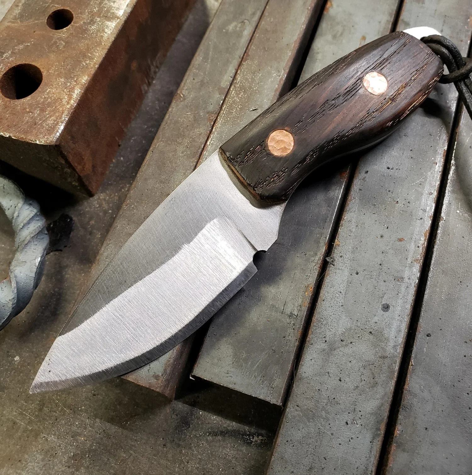 A partially finished knife with a wooden handle and metal blade resting on a metal workbench in a workshop.