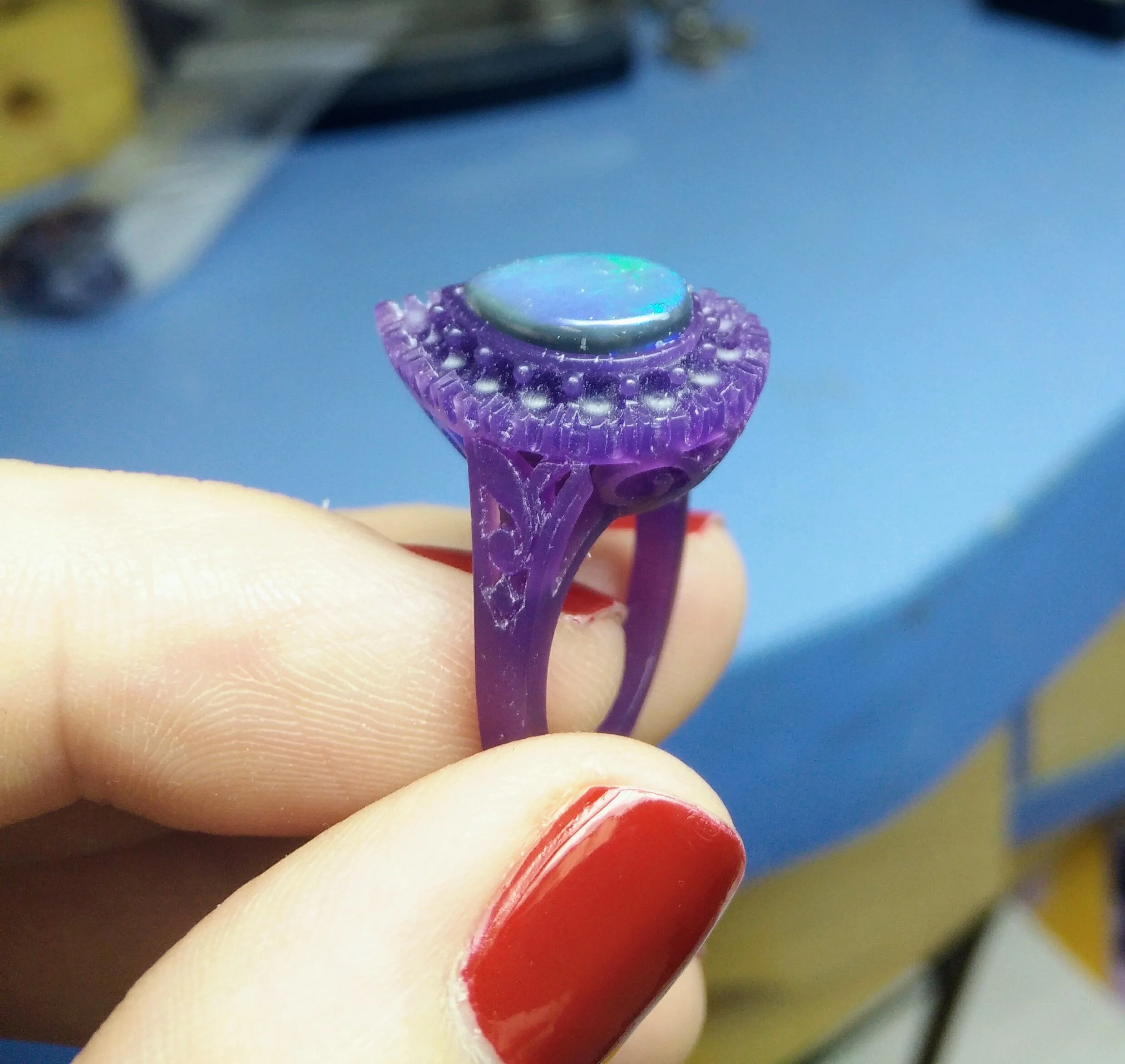 Hand-carved purple jewelry wax model of a gemstone ring, held by a jeweler during the bespoke design process.