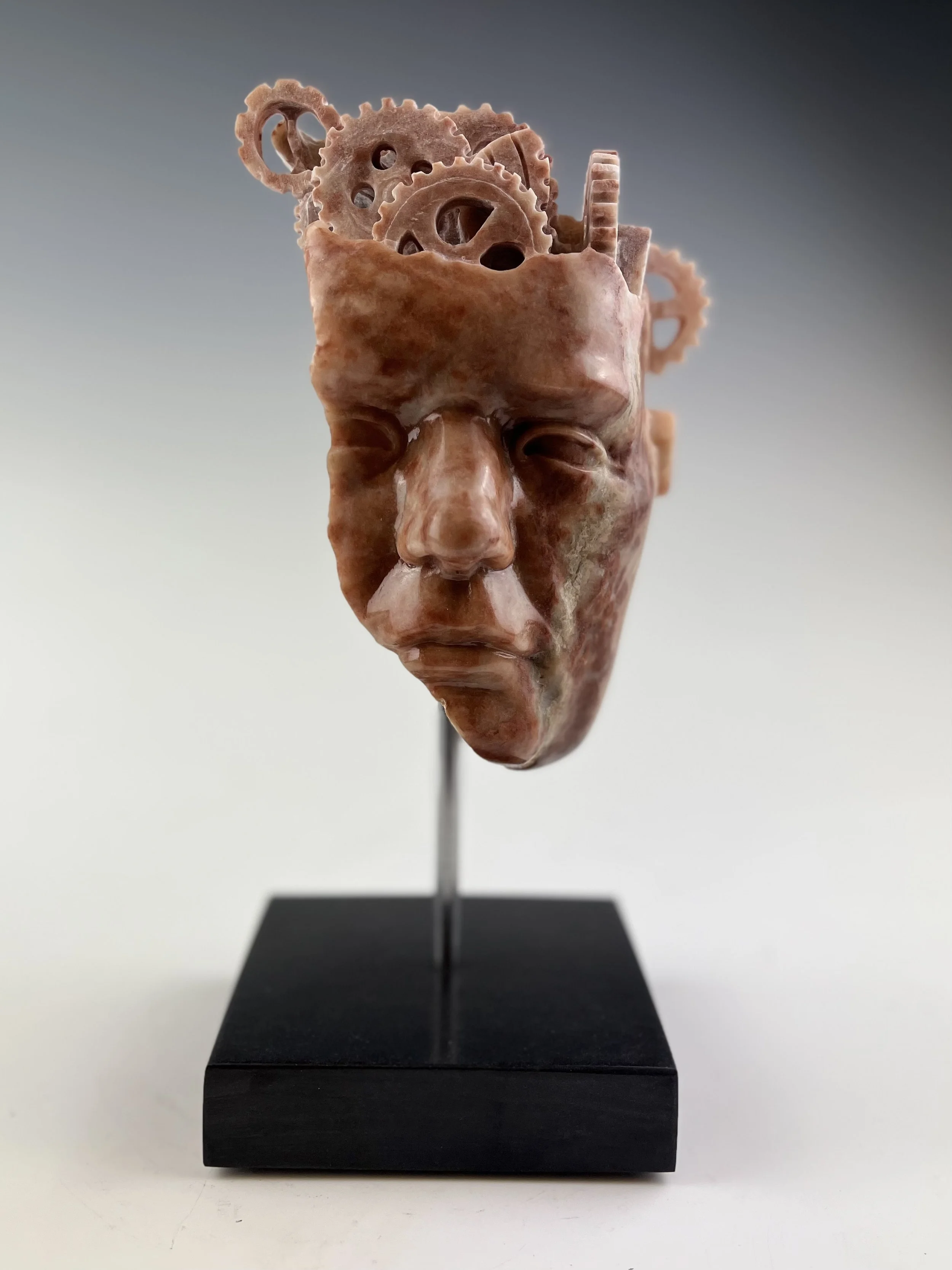 Time Spent In My Brain is a red alabaster sculpture of a human face with carved gears in the back of the head