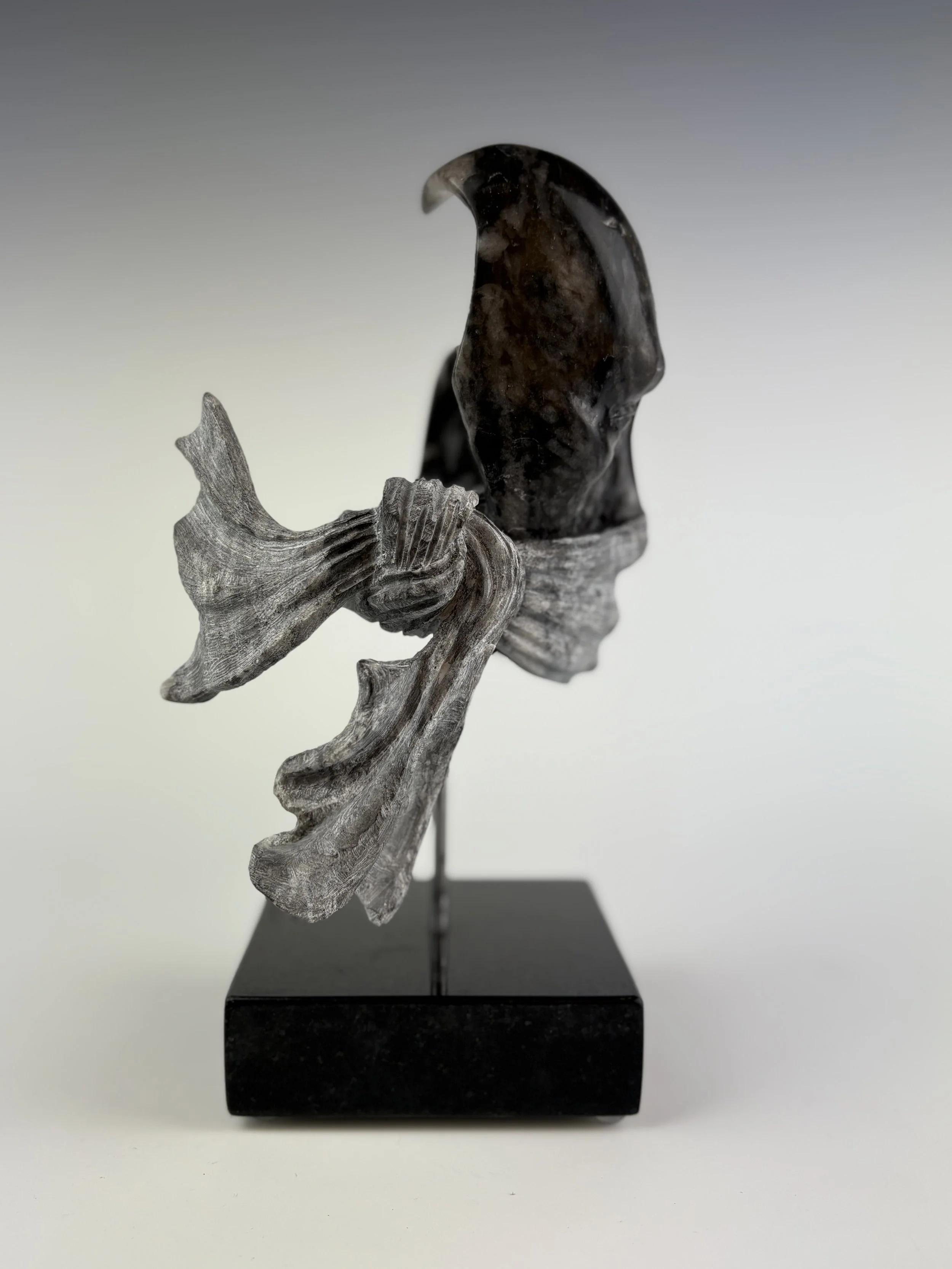 Black soapstone sculpture of a partial face with a carved mask over the mouth