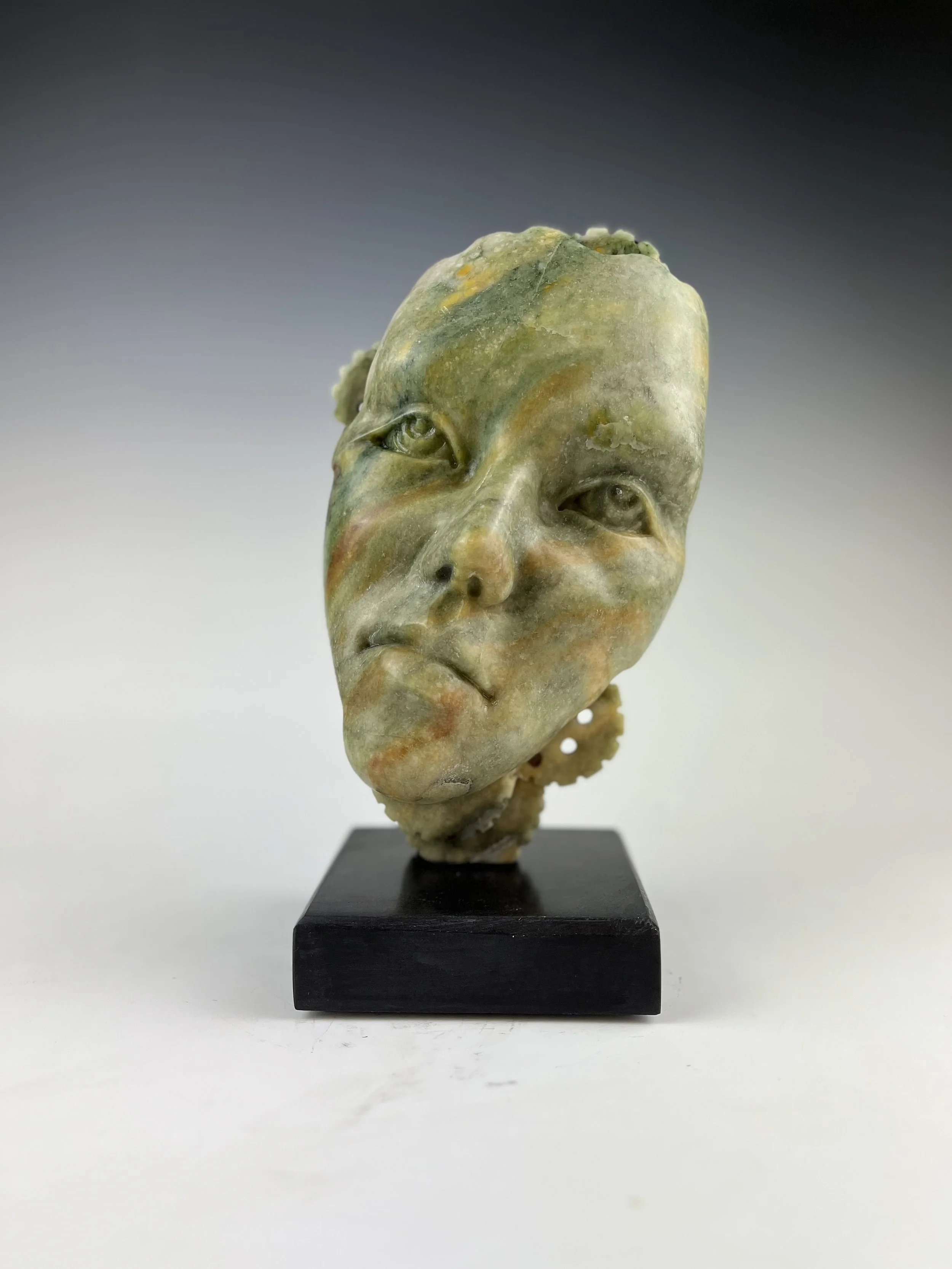 They Influence How We Think is an alabaster sculpture that is a human face with gears and a small figure on the back of the head.