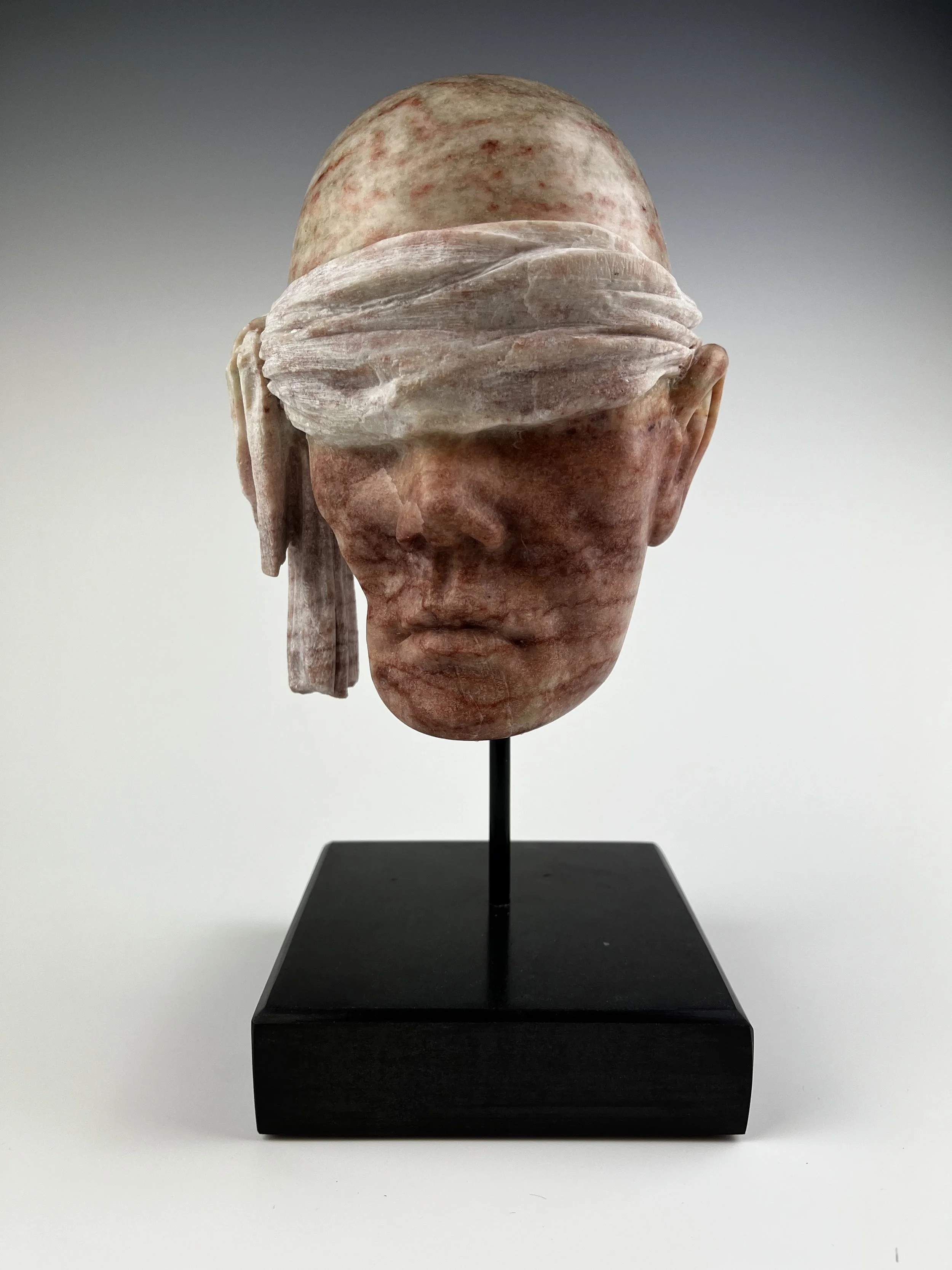 Society's Decay - Corrupted Justice" is an alabaster sculpture that has a face with a carved blindfold covering the eyes.