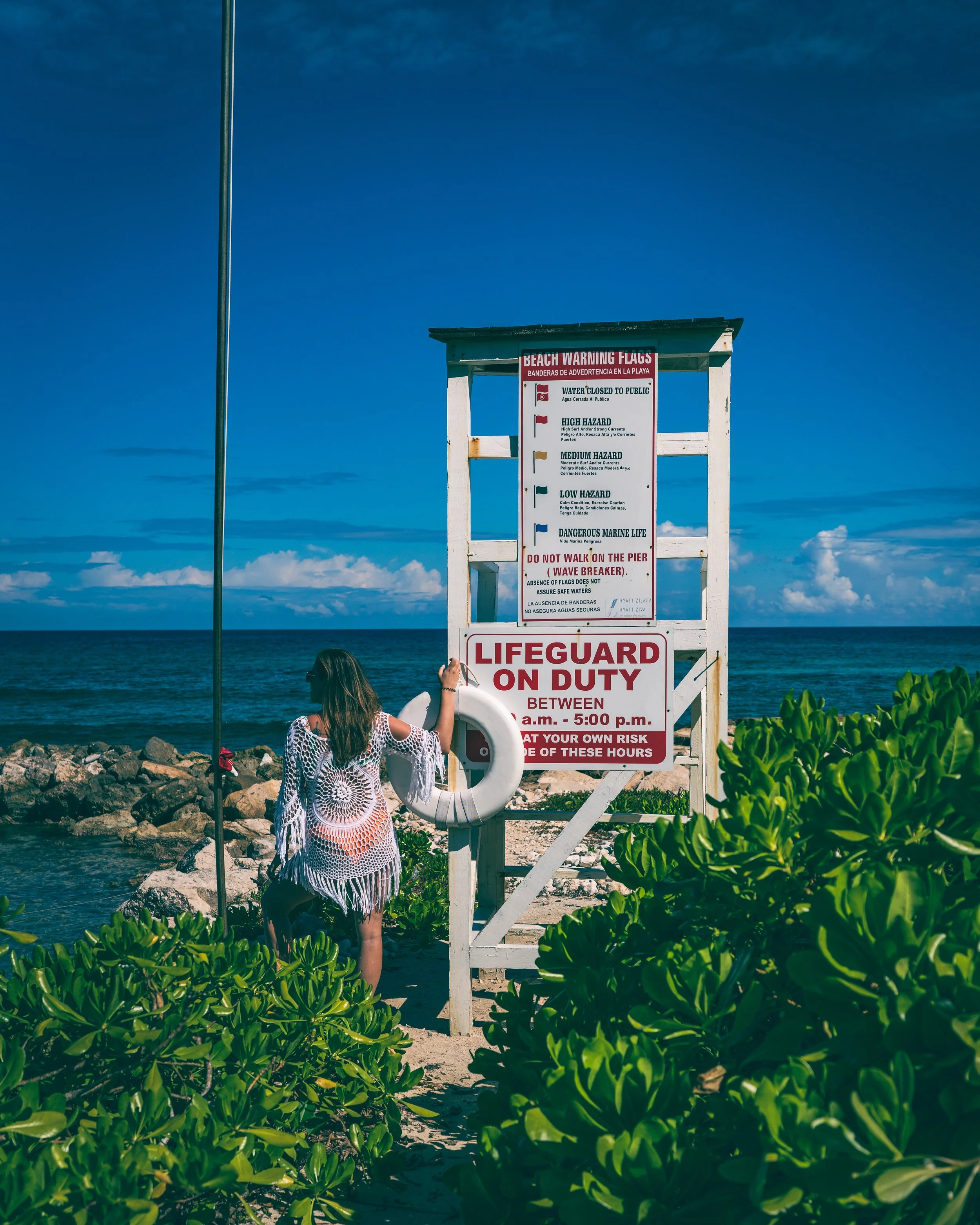 Lifeguard tower at the beach , with ocean and sky in the background and green foliage in the foreground.