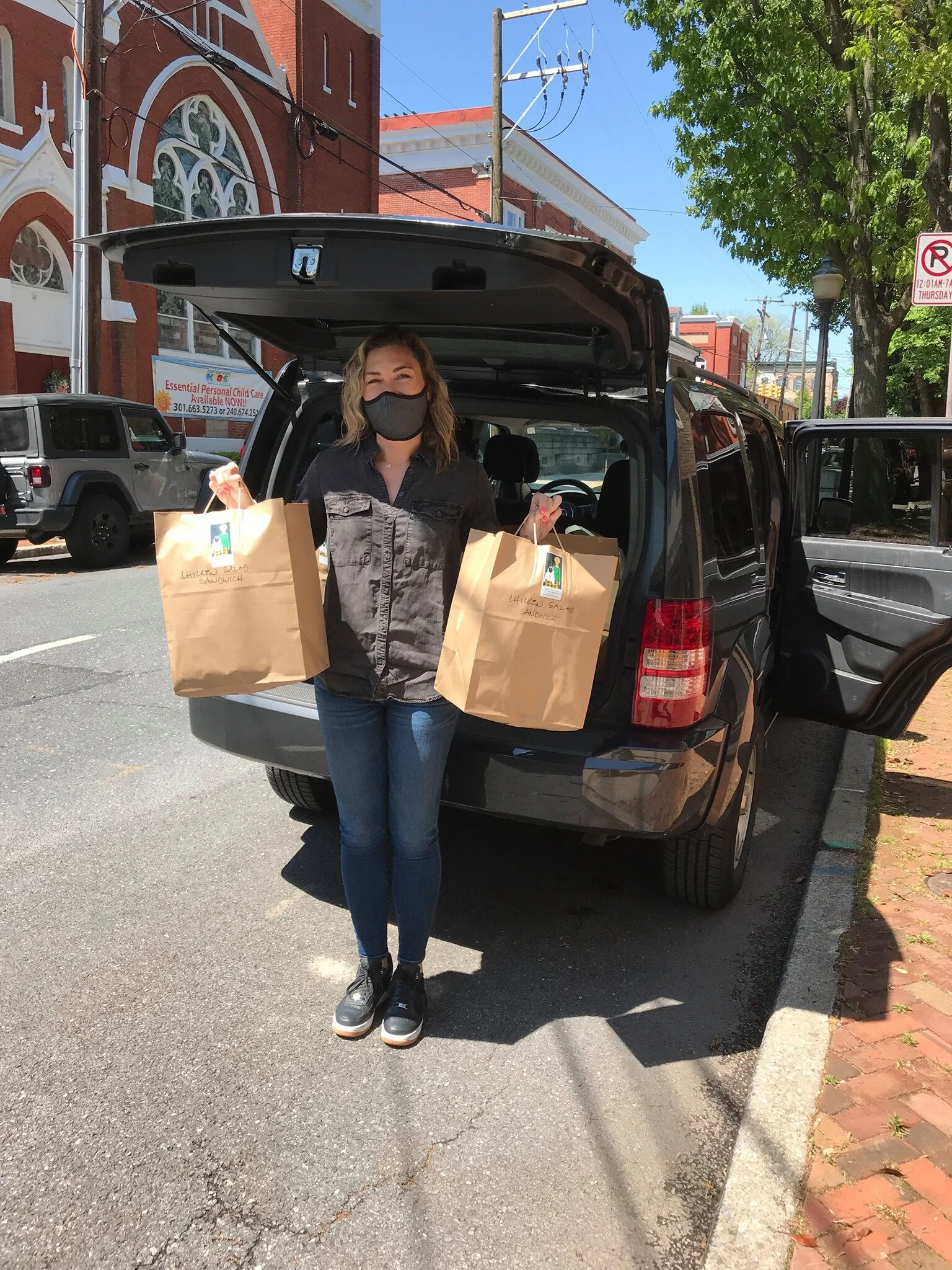A person wearing a dark shirt and jeans holds two brown paper shopping bags in front of the open trunk of an SUV..jpg