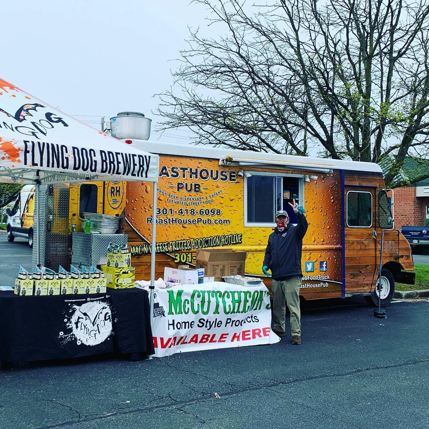 A man waves from the window of a food truck branded "Easthouse Pub" parked next to a tent for "Flying Dog Brewery" and a table displaying "McCutcheon Home Style Products.".jpg