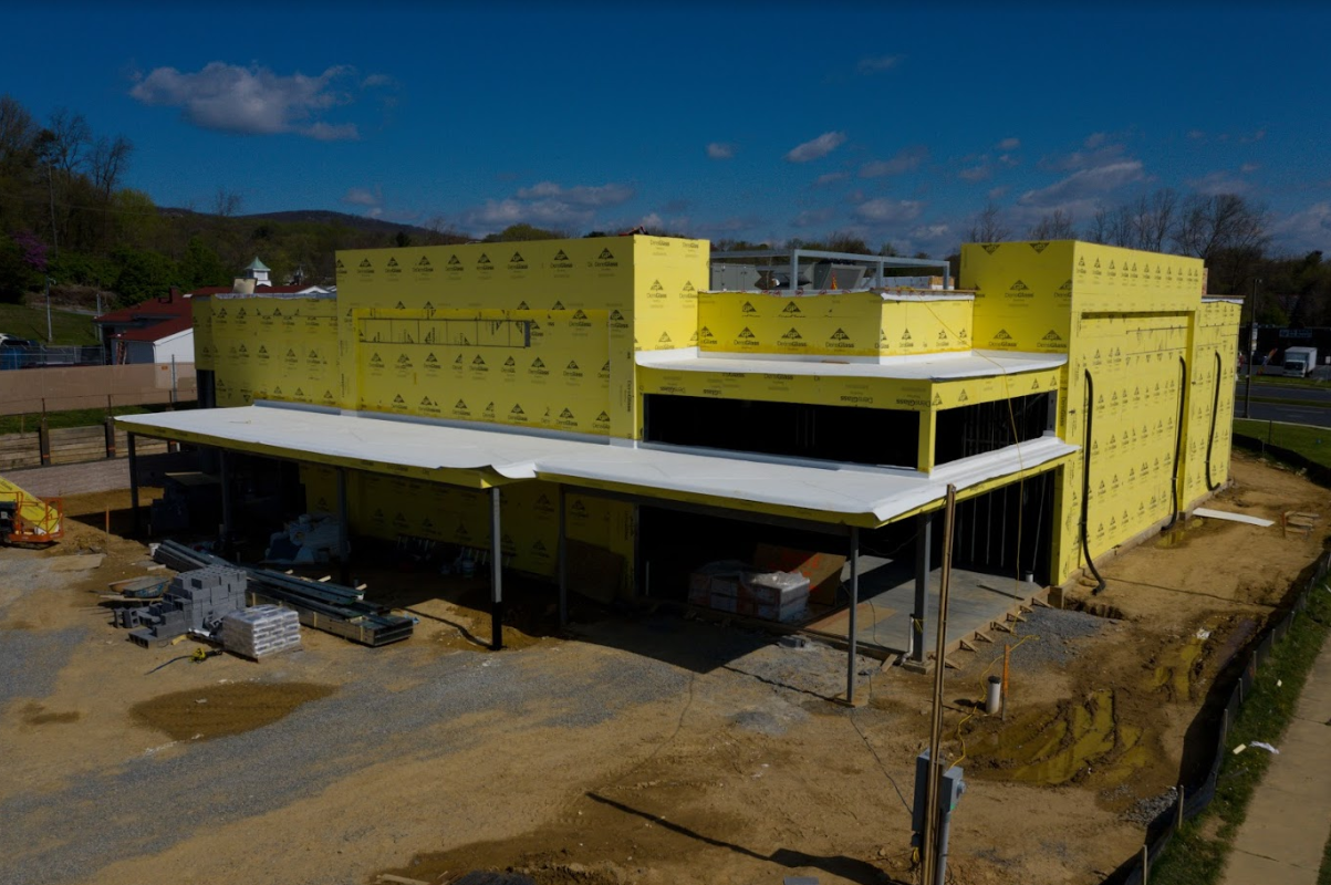 Exterior view of a large building under construction, with yellow sheathing covering most of the walls and white material on the roof..png