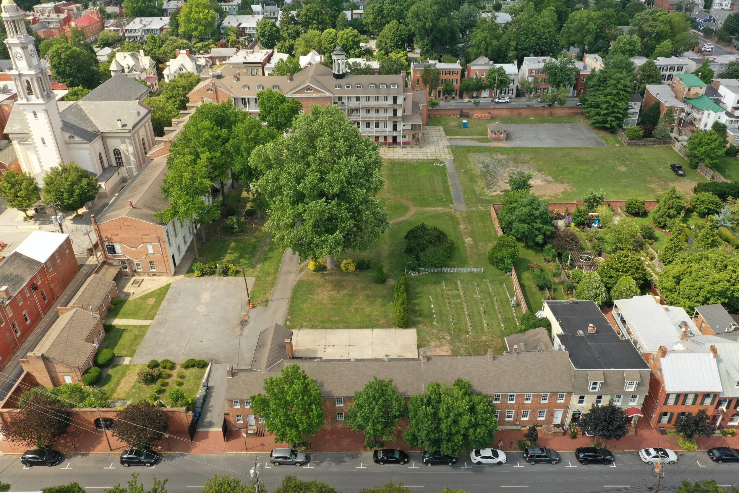 Aerial view of a historic town with a church steeple, brick buildings, a large green lawn, and several trees..jpg