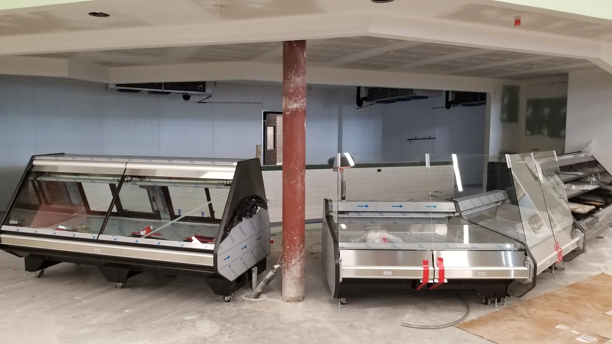 Several empty, stainless steel and glass refrigerated display cases are installed on casters in a retail space under construction..jpg