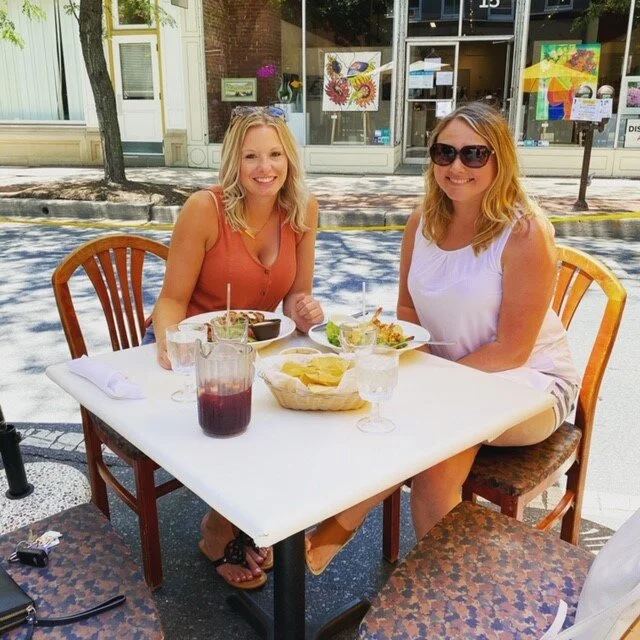 two women seated at table outdoors with food and drink