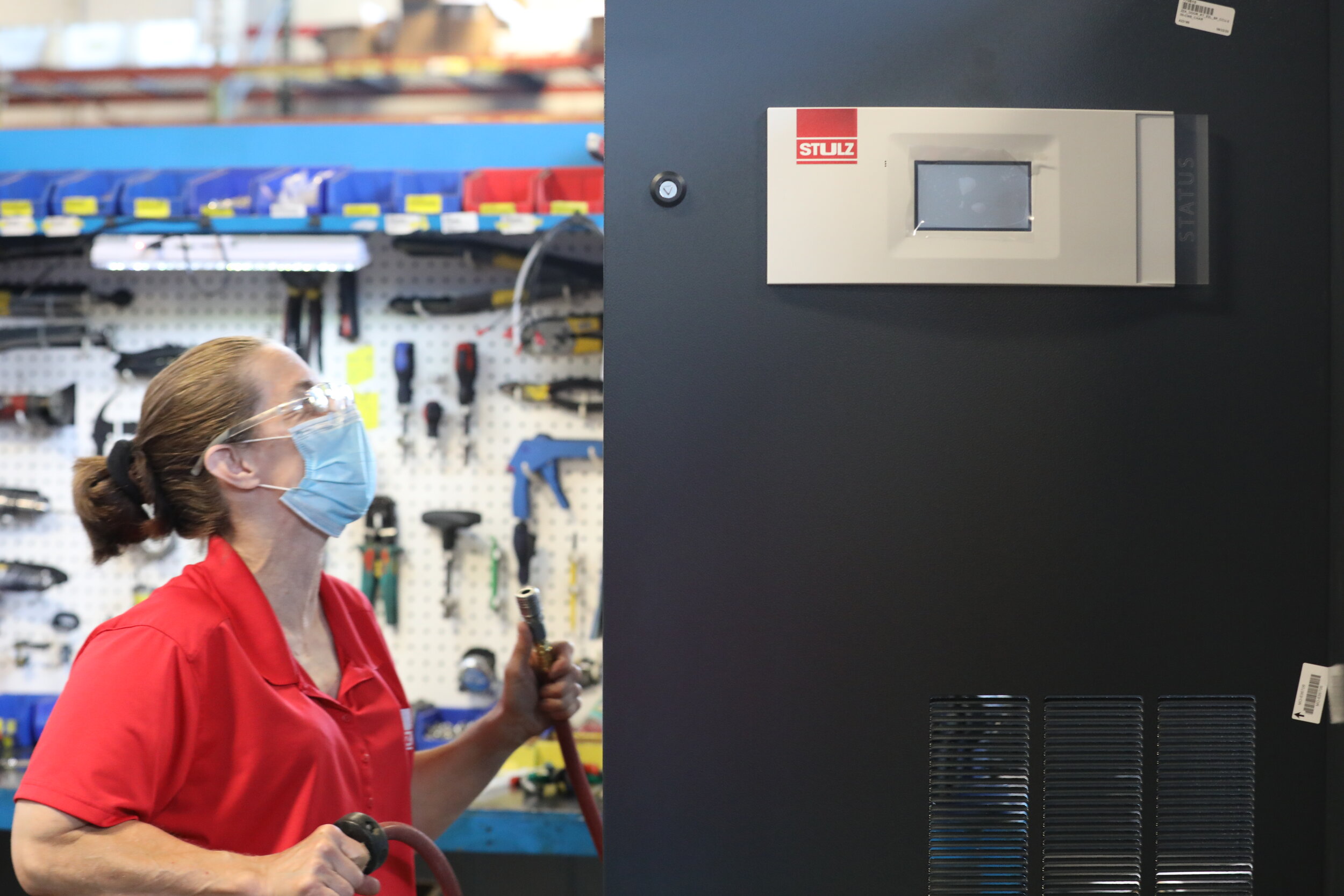 A woman in a mask and gloves stands before a large black cabinet, indicating a focus on safety and hygiene..JPG