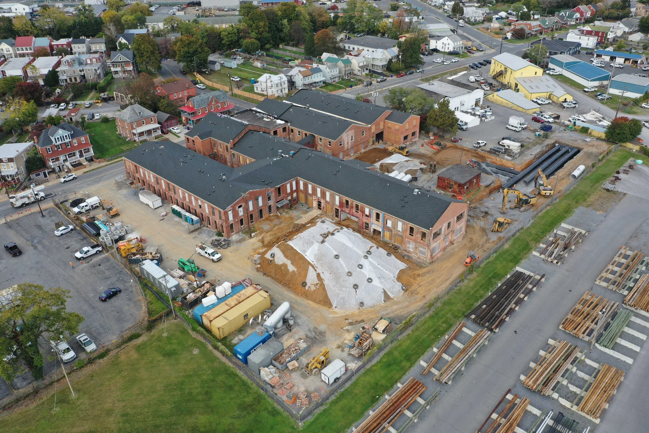 Aerial view of a large brick building under construction in a suburban area. Surrounding it are parked vehicles, construction materials, and nearby houses..jpg