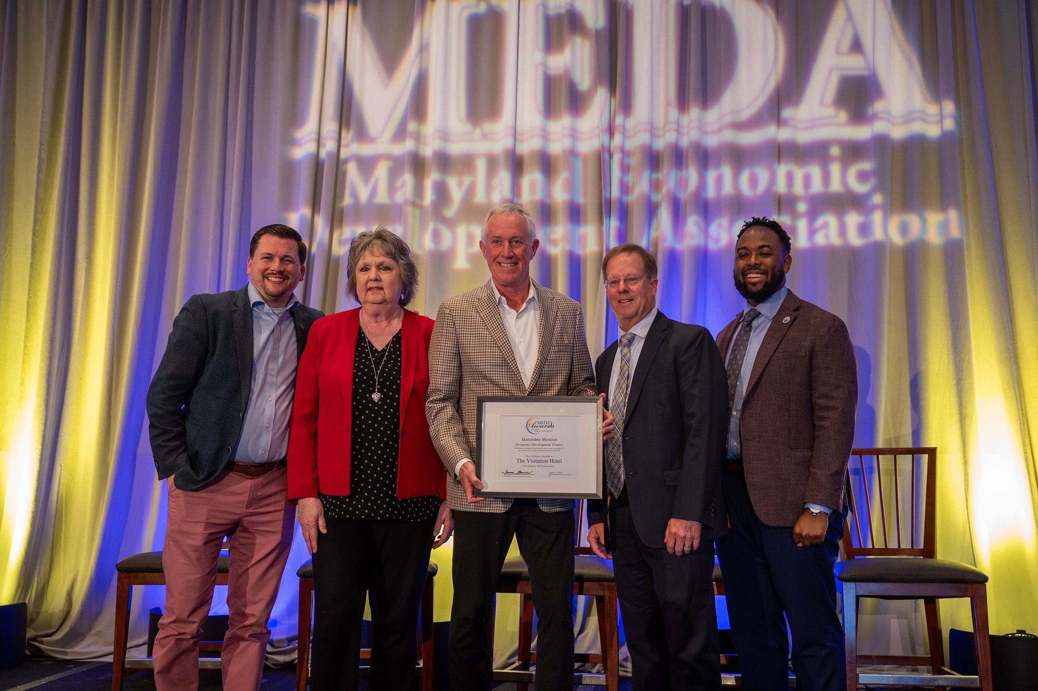 group of people standing on stage for picture holding award in front of curtains that read MEDA in lights