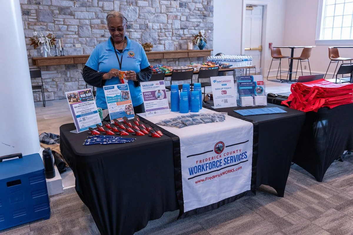 woman standing behind exhibitor booth that reads "Frederick County Workforce Services."