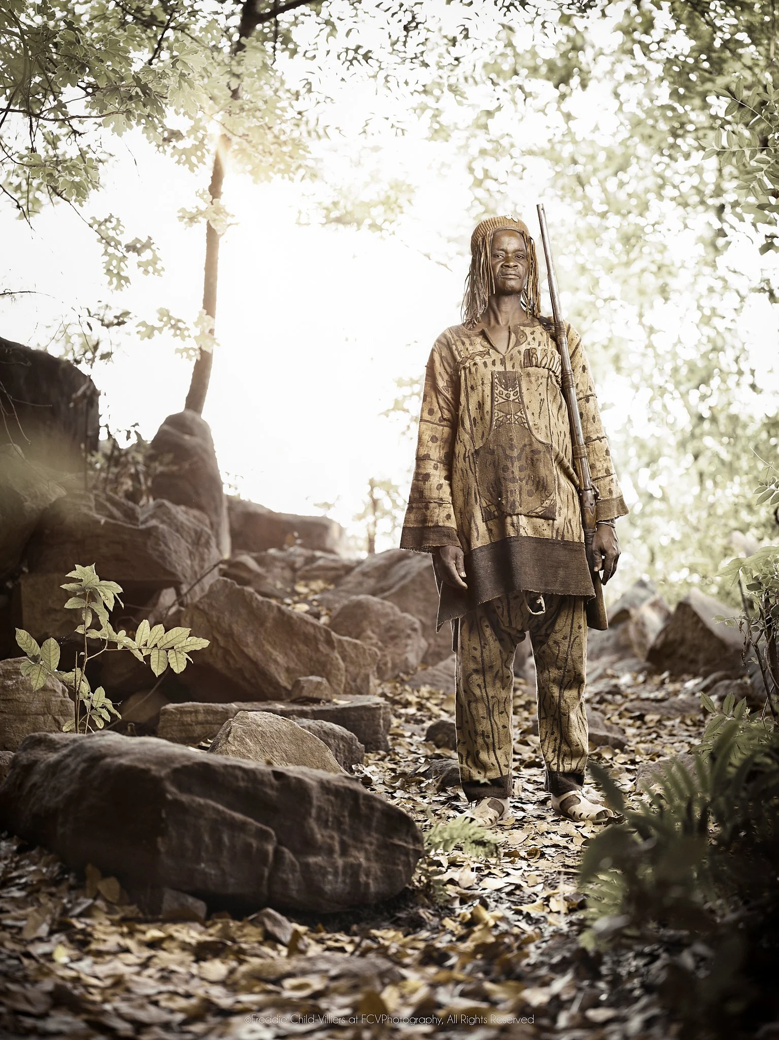 Bandjougou standing among rocks and trees in a shaded green valley.